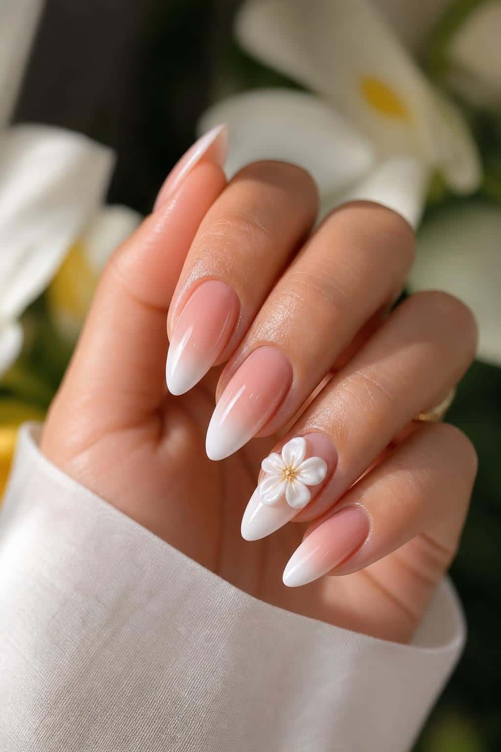 Long almond nails with a pink-to-white ombre French fade and a 3D white flower accent.