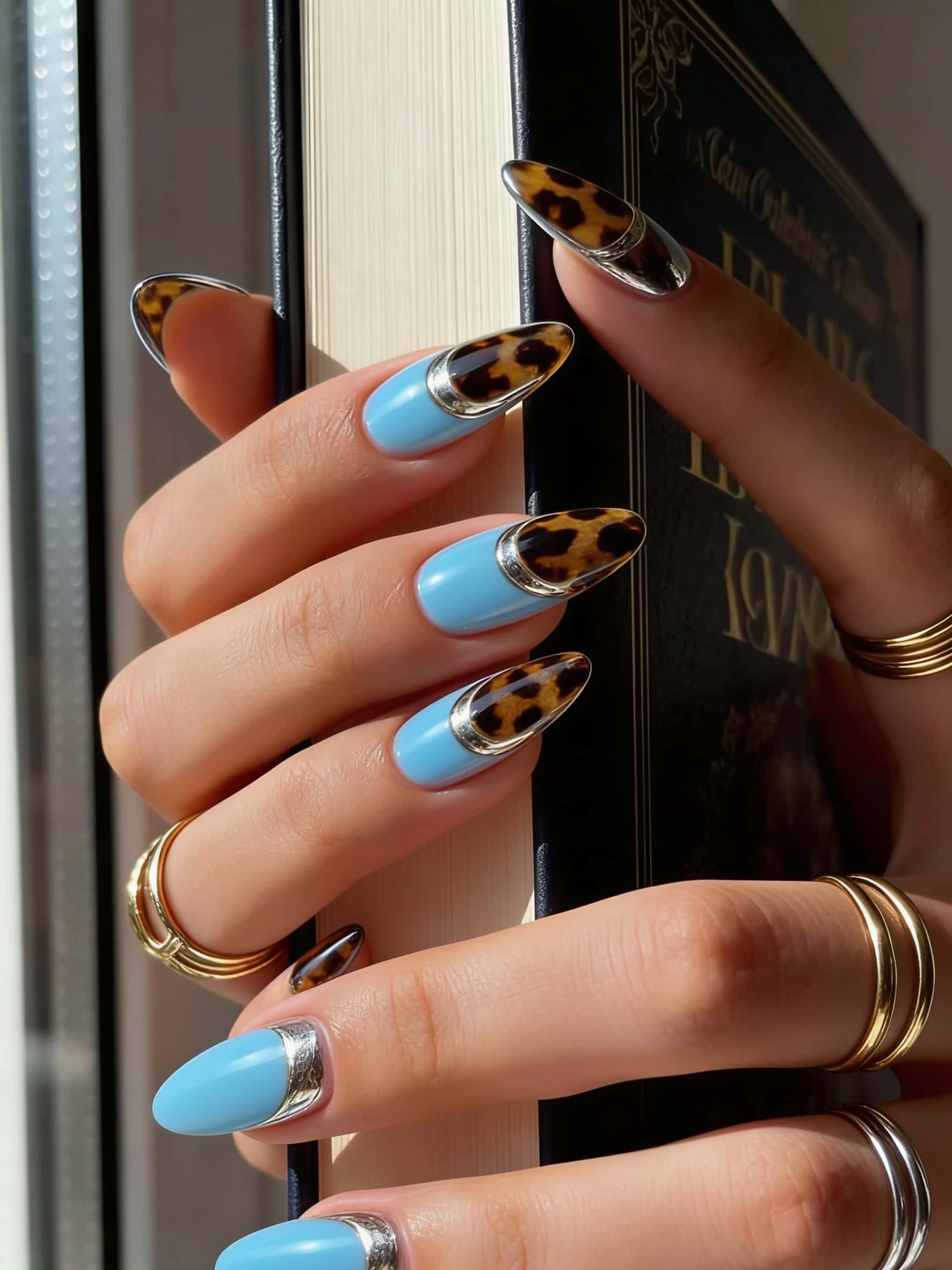Long almond nails with a sky blue base, leopard print tips, and silver metallic accents.
