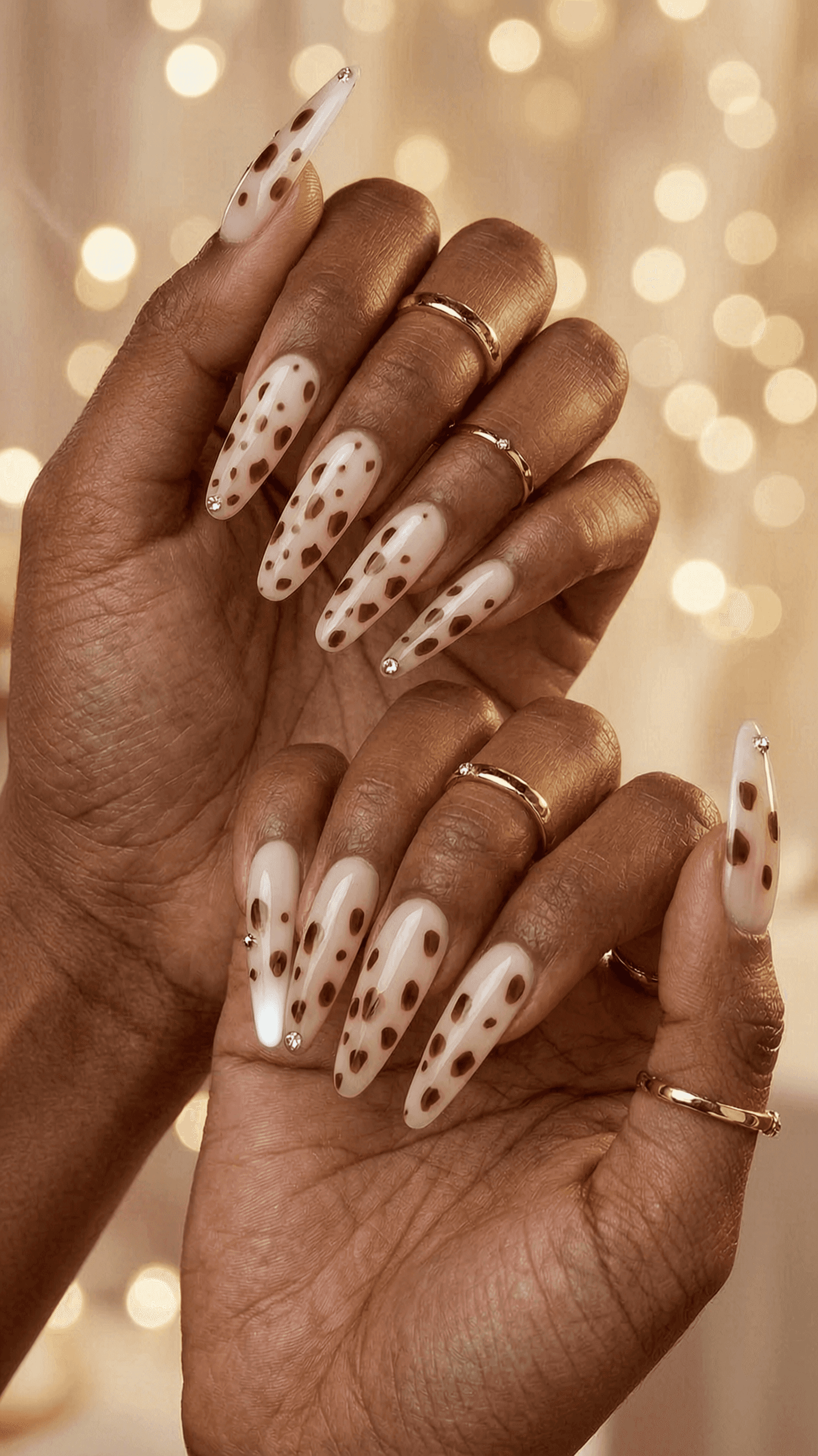 Long stiletto nails with brown dots and rhinestones on a glossy finish.
