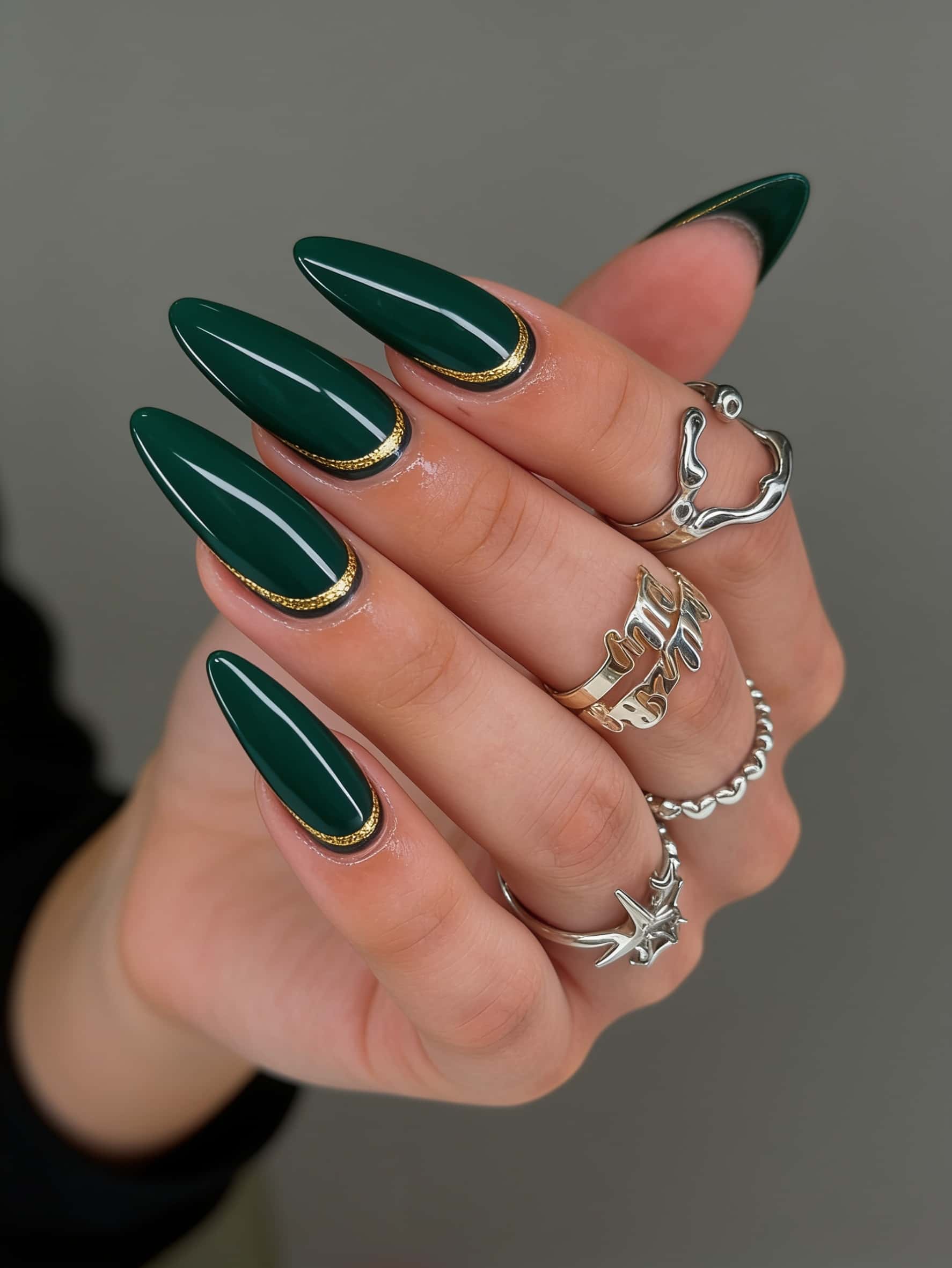 Long stiletto nails in dark green with gold accent and glossy finish.