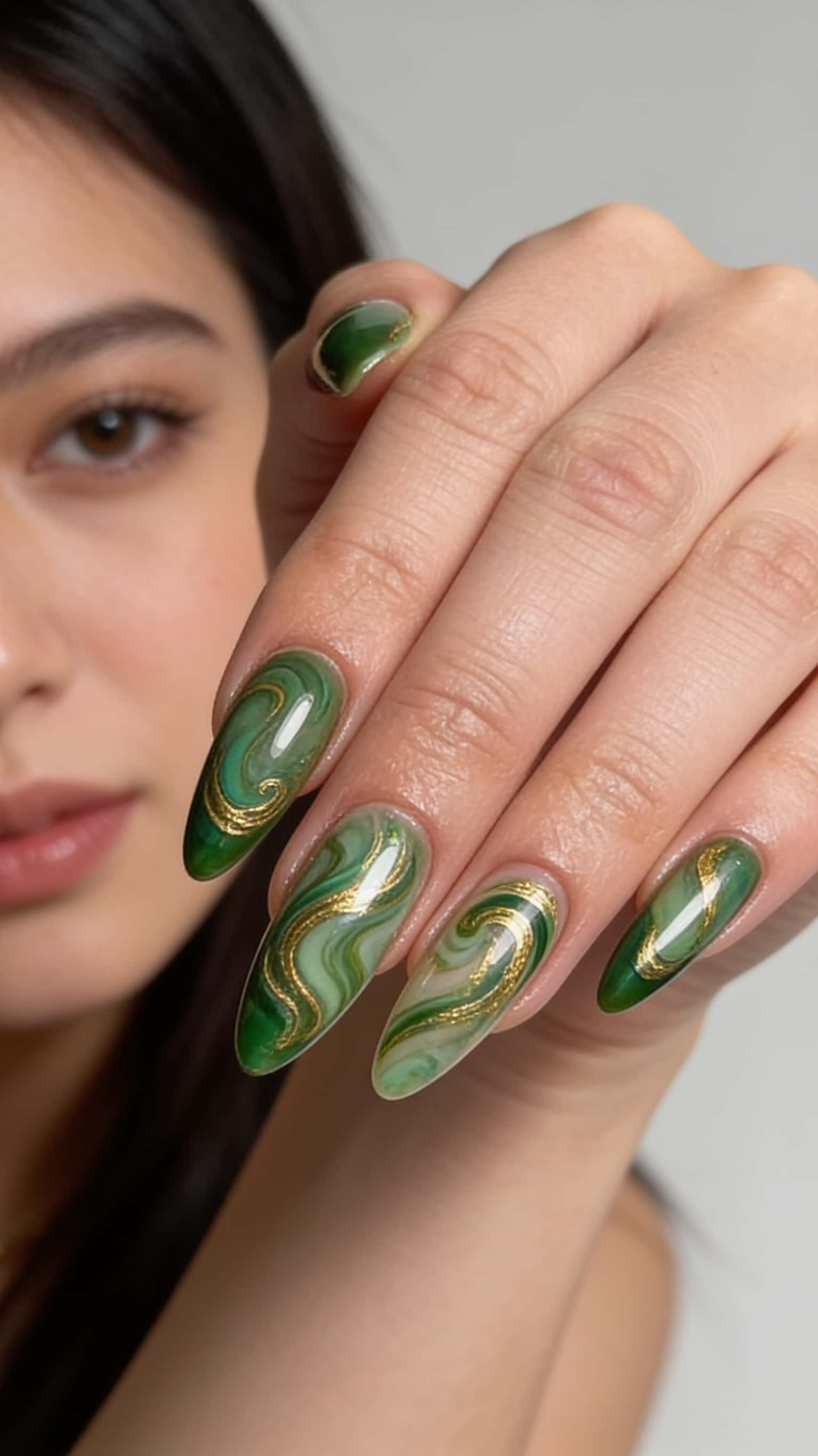 Long stiletto nails with a green marble swirl design and gold glitter accents.