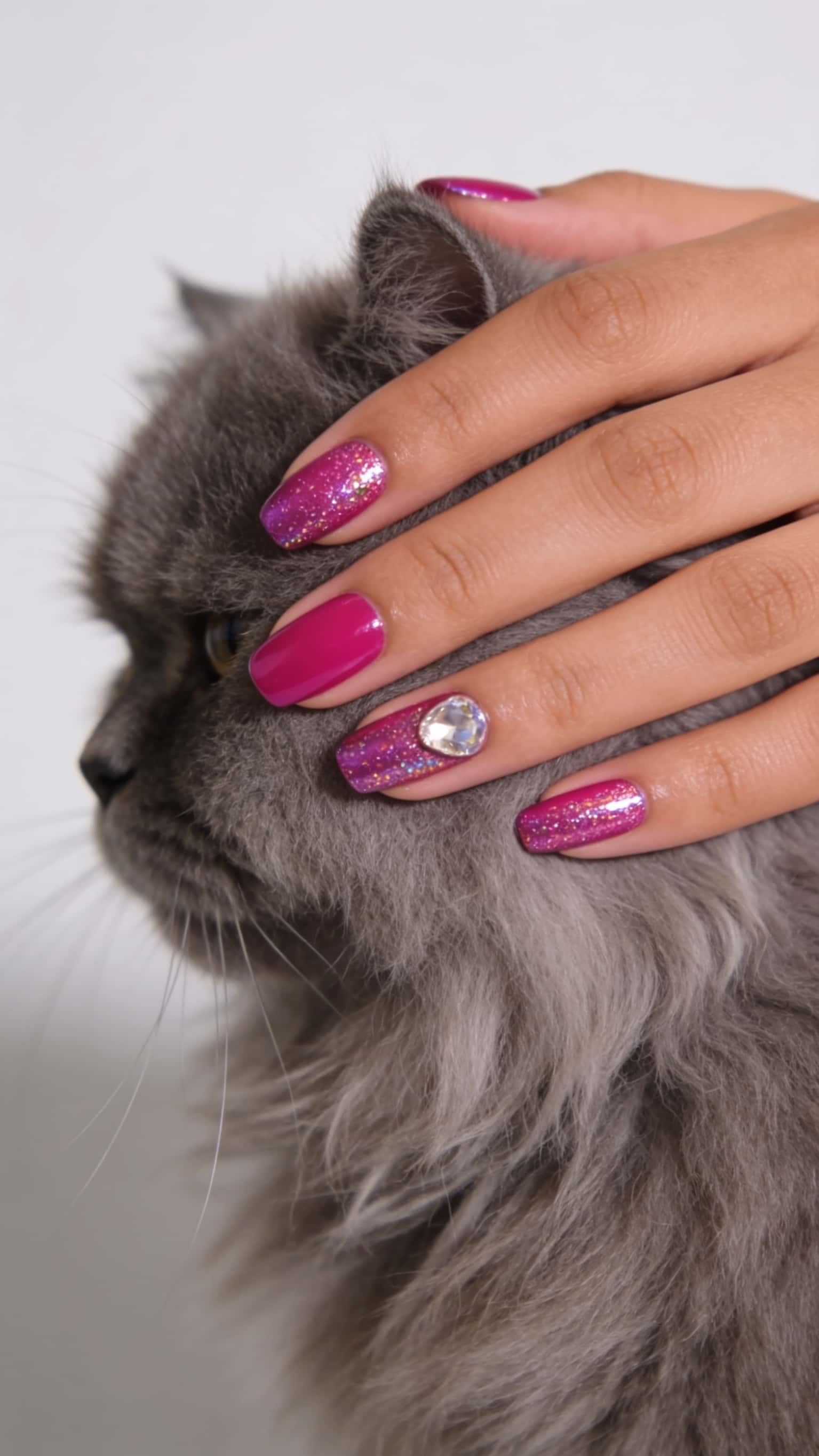 Short oval nails with a mix of fuchsia solid and glitter polish, accented with a clear oval gem.