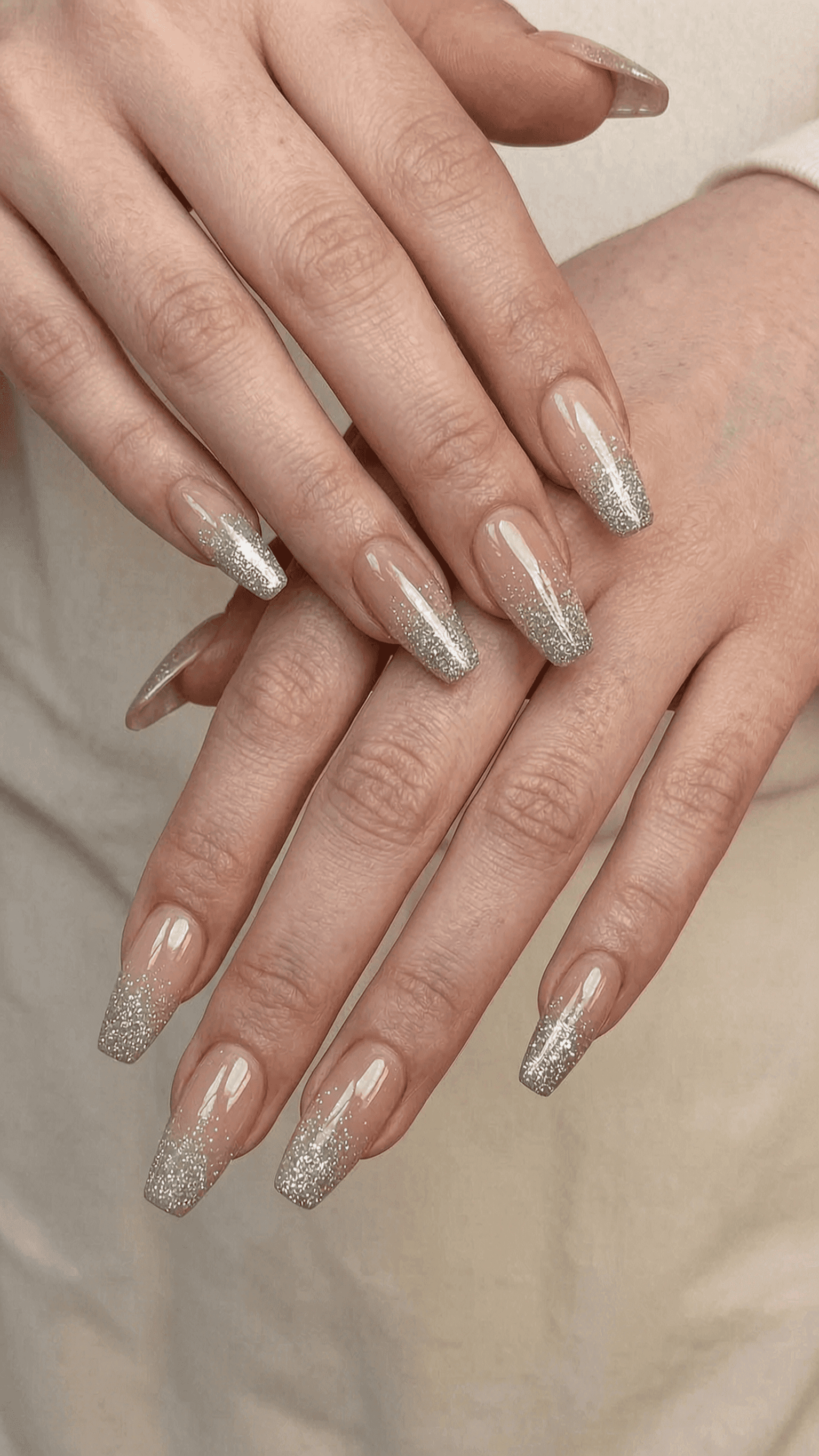Long coffin nails with a sheer nude base and silver glitter ombre tips.