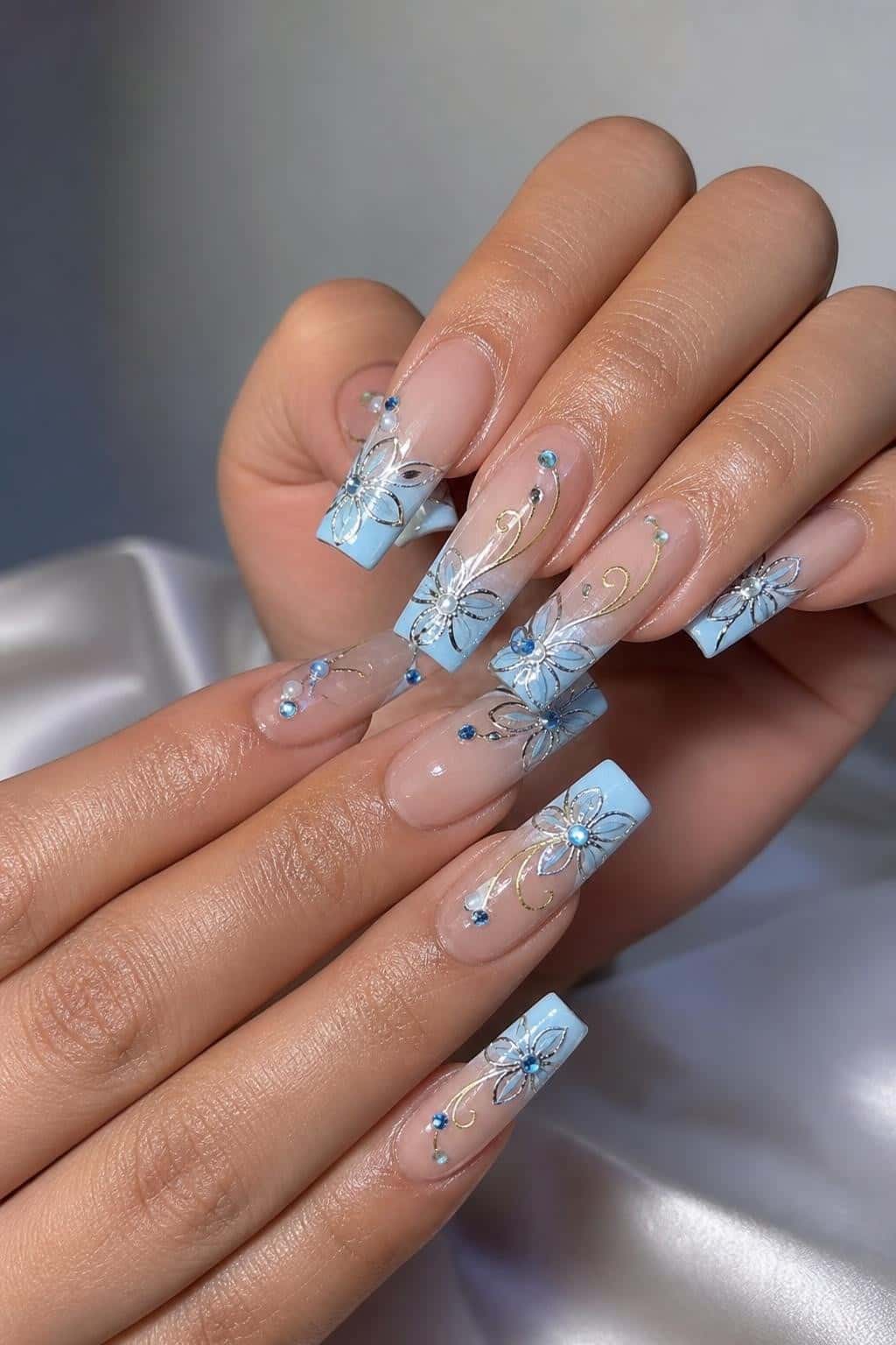 Long blue glitter stiletto nails with floral design and rhinestones.