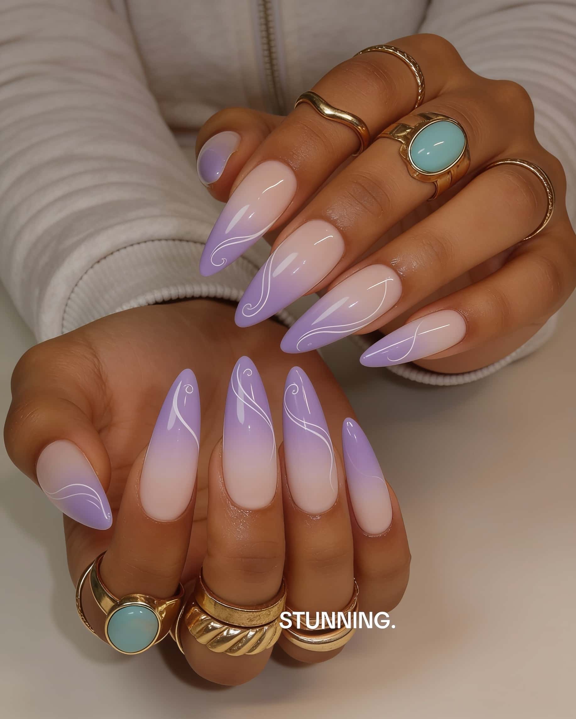 Long stiletto nails with a nude to lavender ombre and white abstract swirl lines.