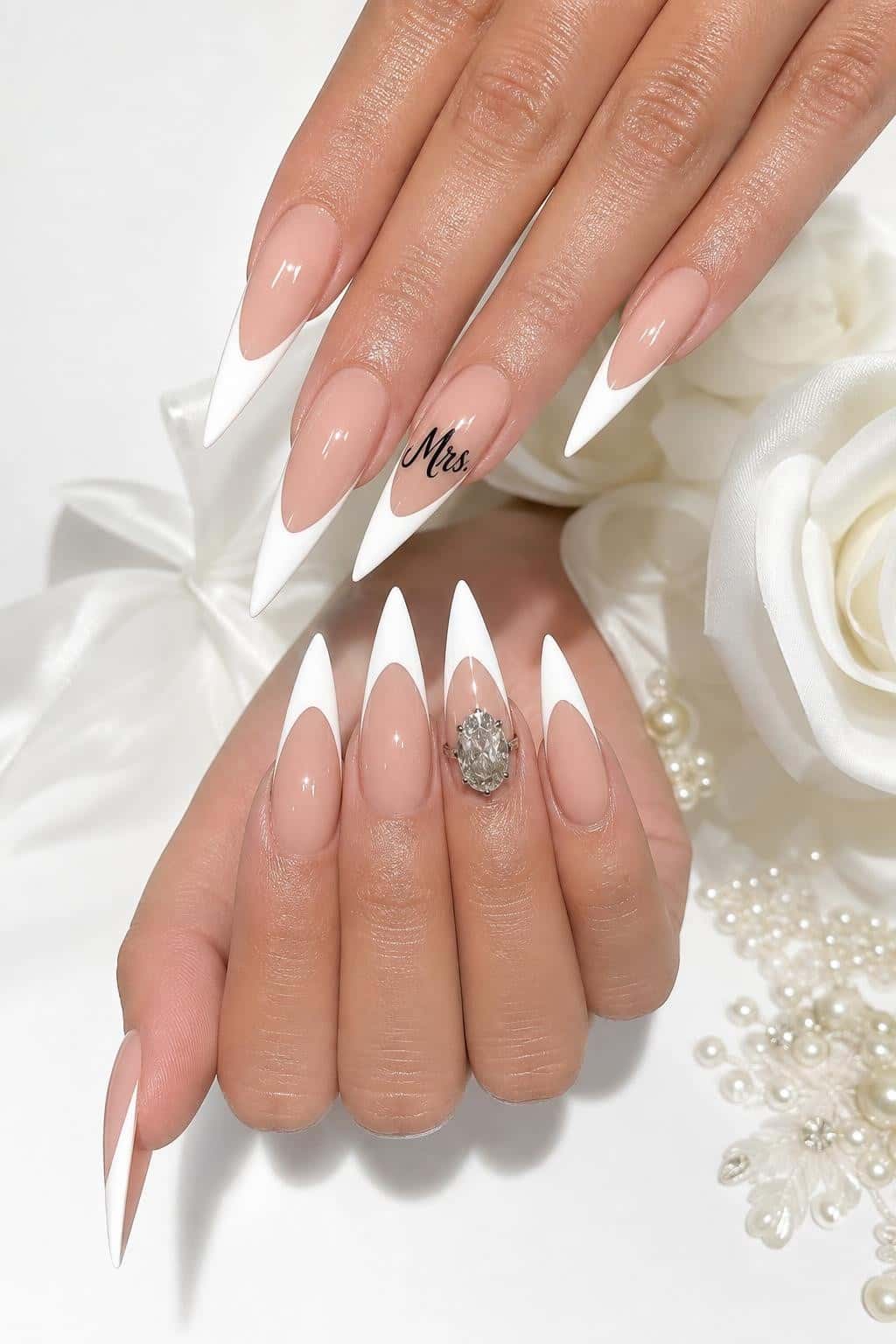 Long stiletto nails with a nude base, sharp V-cut white French tips, and 'Mrs.' script on one nail.