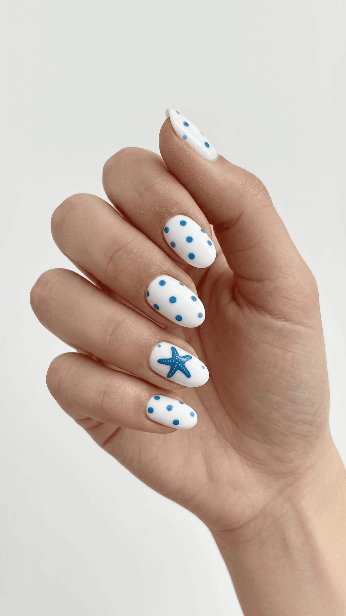 Oval nails with a white base, blue polka dots, and a blue starfish accent nail.
