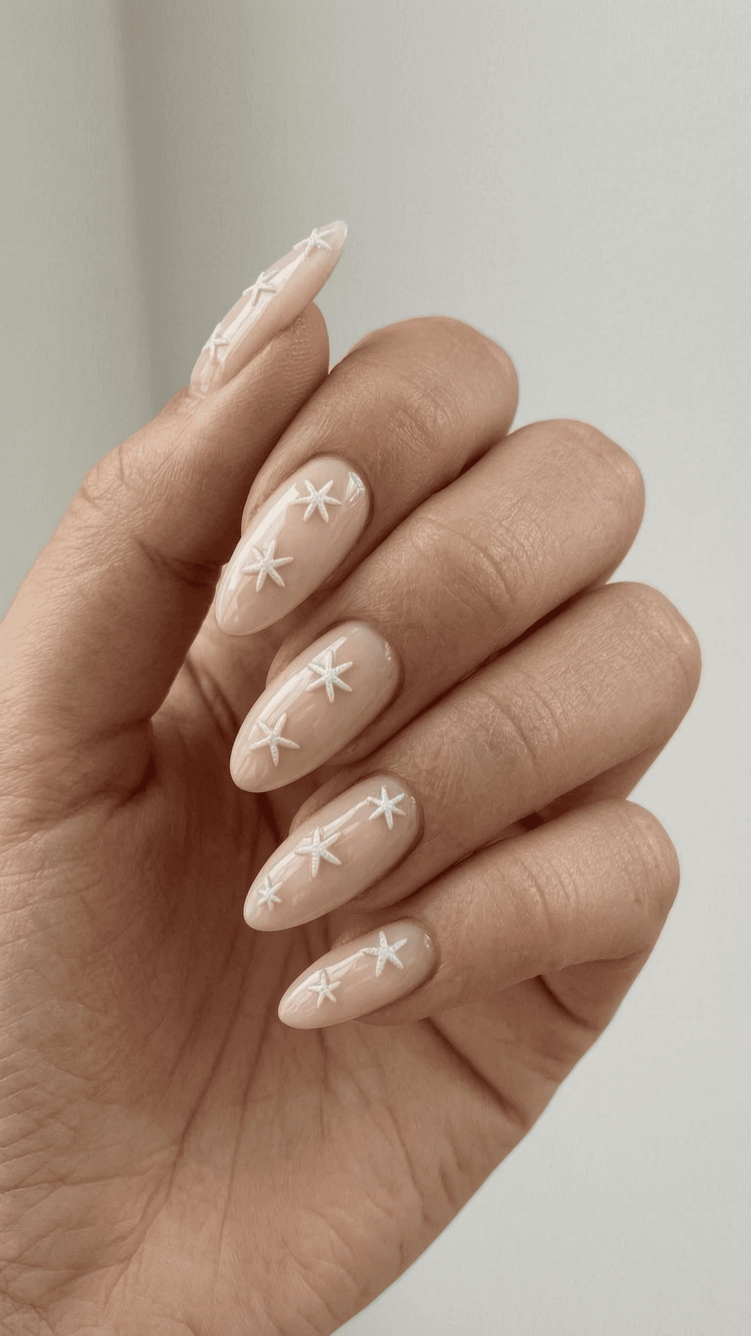 Long almond nails with a sheer nude base featuring white 3D star embellishments.