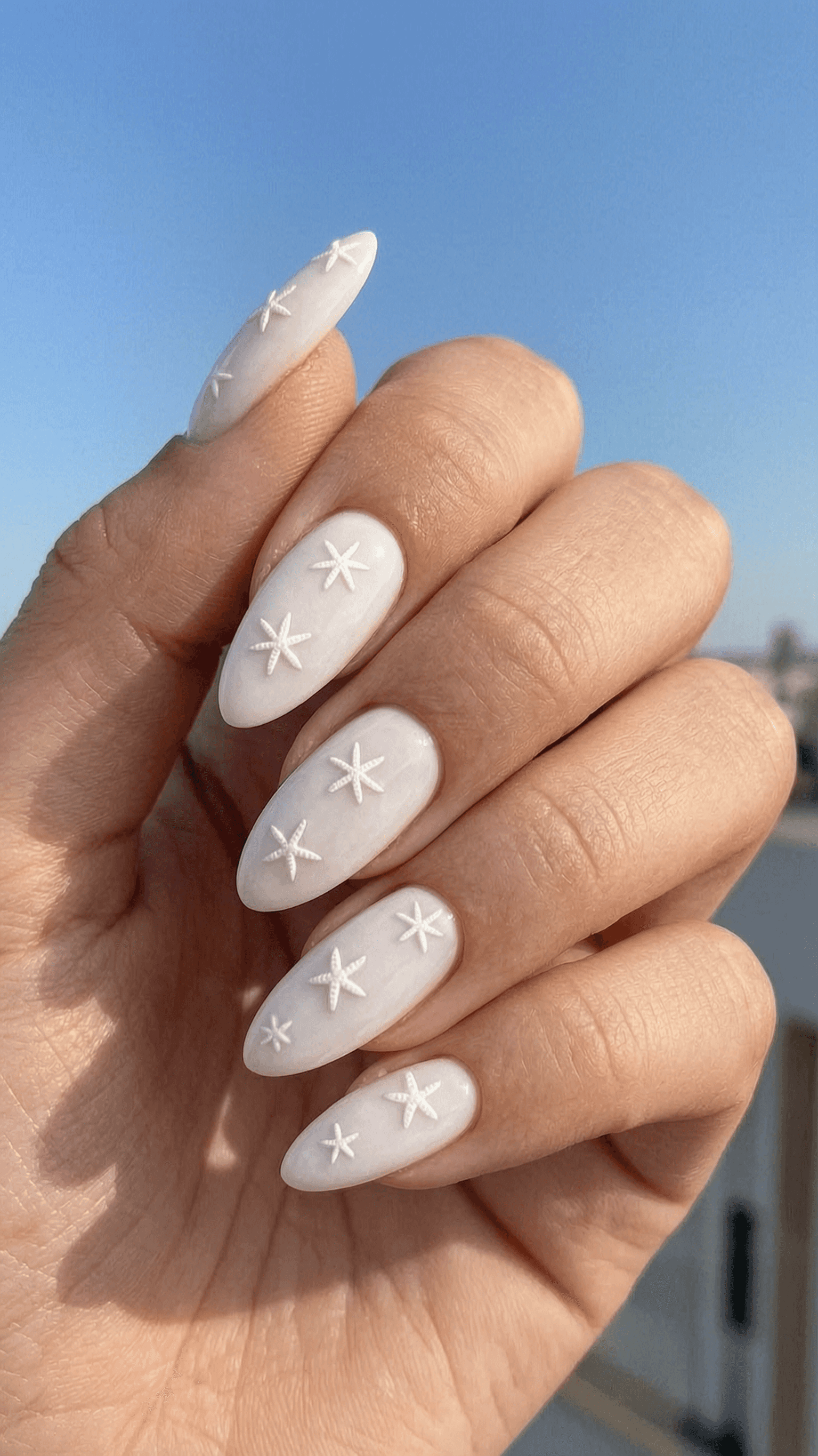 Long milky white almond nails with 3D starfish art and glossy finish.
