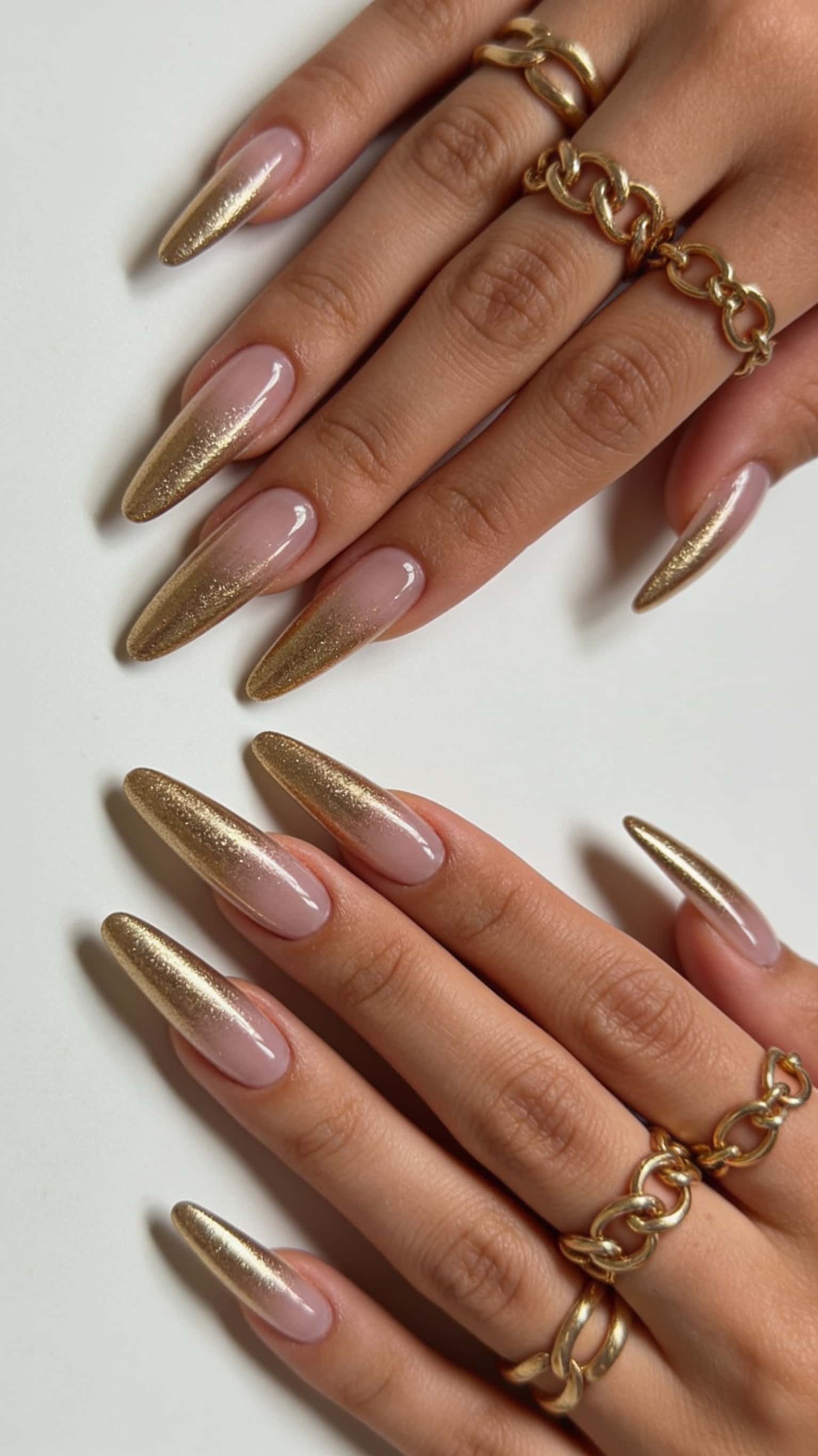 Long almond nails with a nude base and shimmering gold glitter ombre tips.