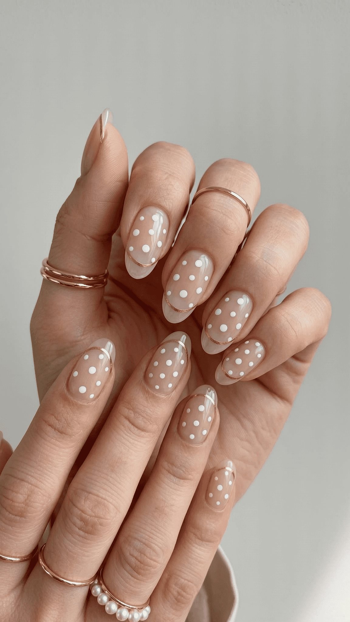 Sheer nude oval nails with white polka dots and a gold accent.