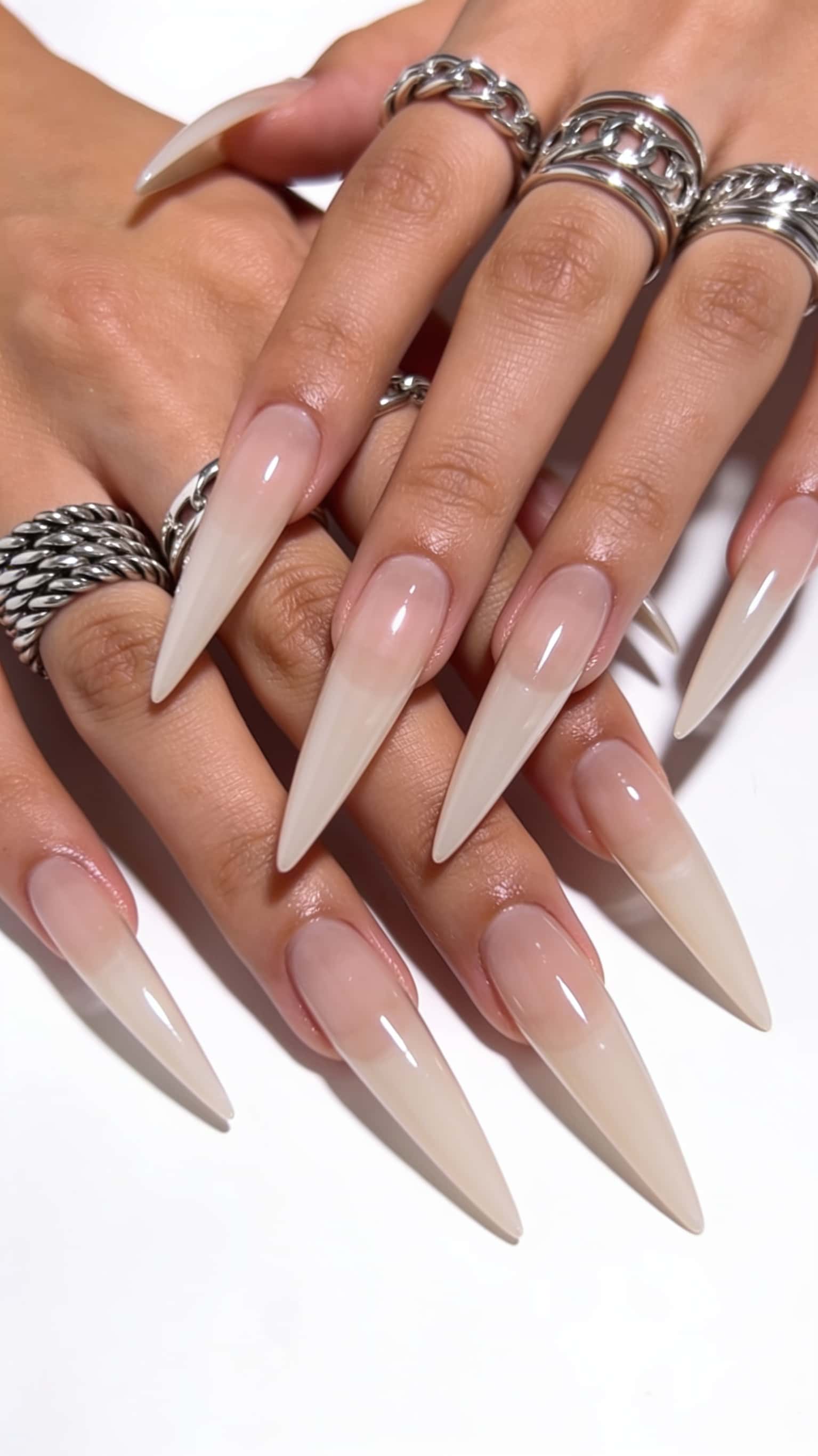 Long stiletto nails with a nude pink base fading into creamy beige tips and a high-gloss finish.