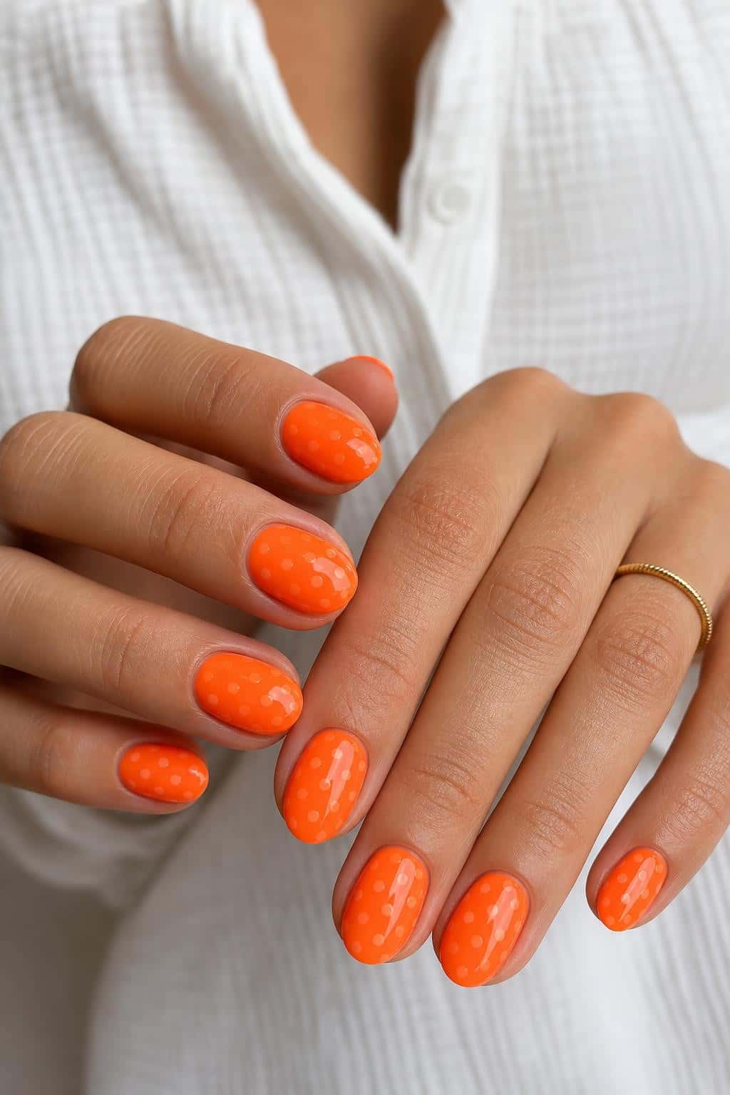 Short oval nails with a glossy orange base and white polka dot pattern.