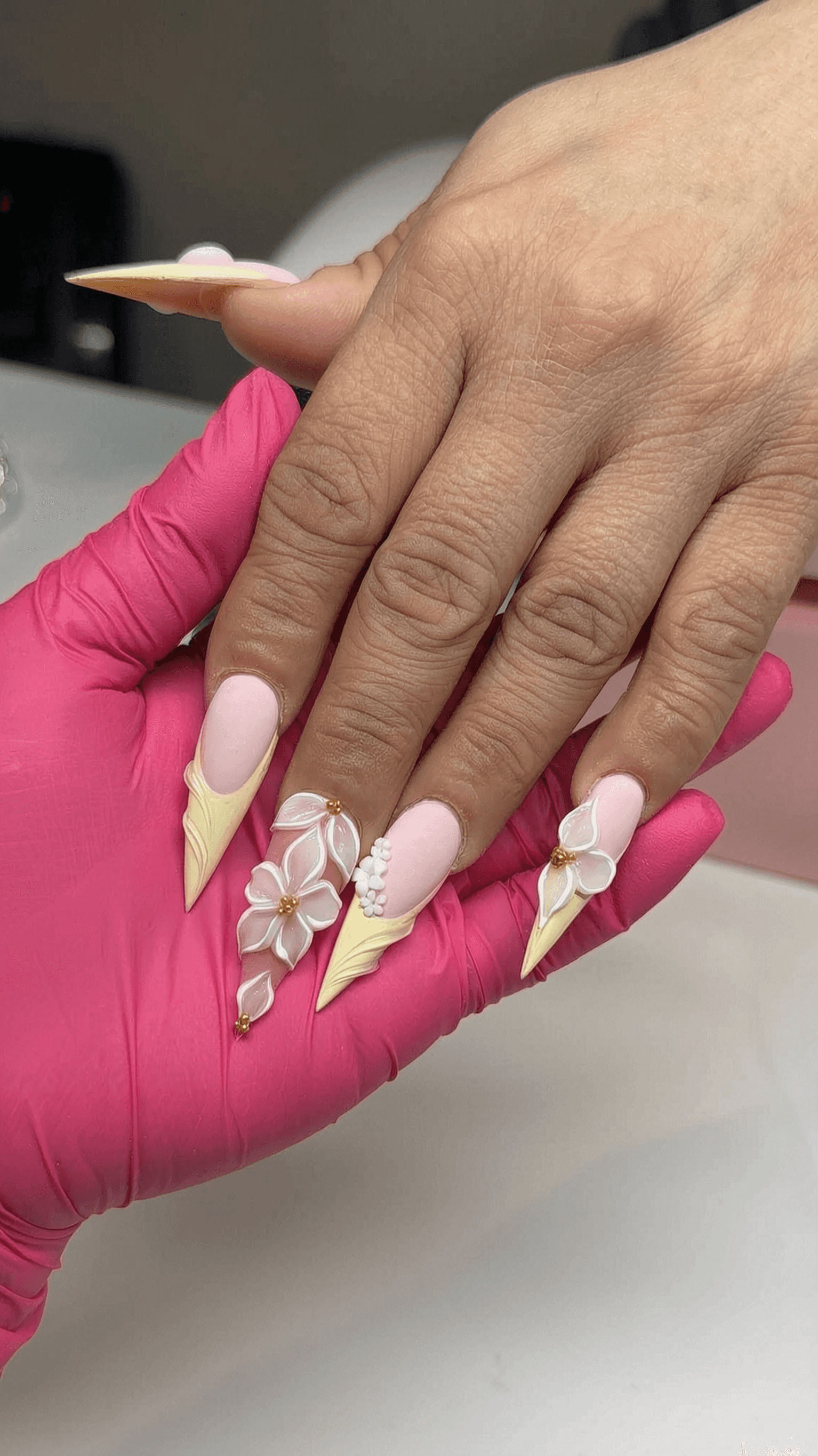 Long stiletto nails with 3D floral design in pastel colors and gold accents.