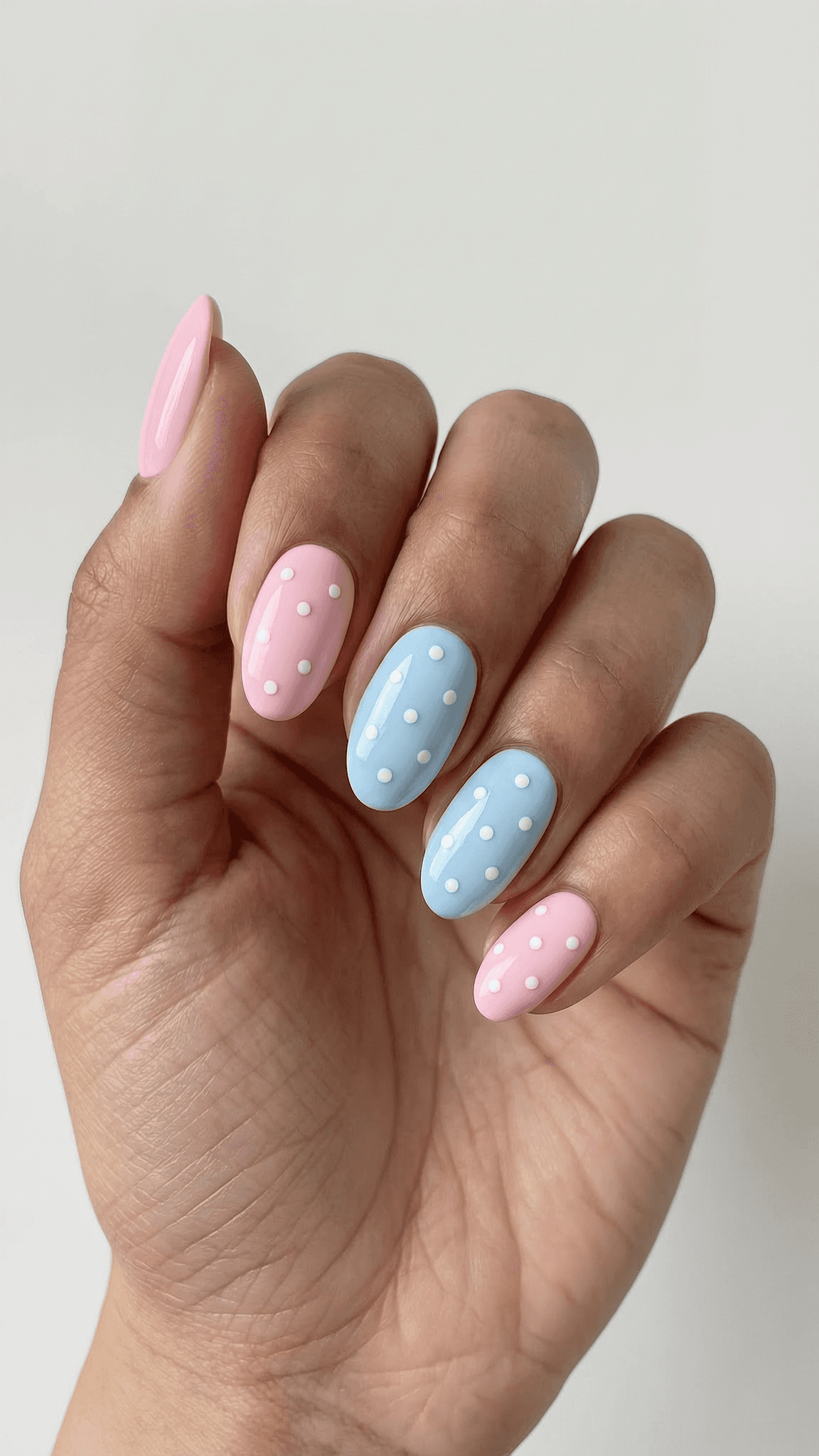 Oval nails with alternating pastel pink and blue bases, each decorated with white polka dots and a glossy finish.