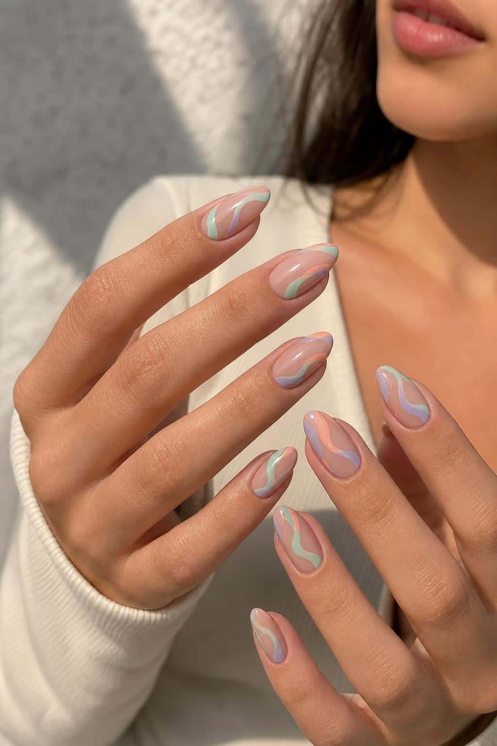 Almond nails with a sheer nude base adorned with pastel wavy lines in mint, peach, and lavender.
