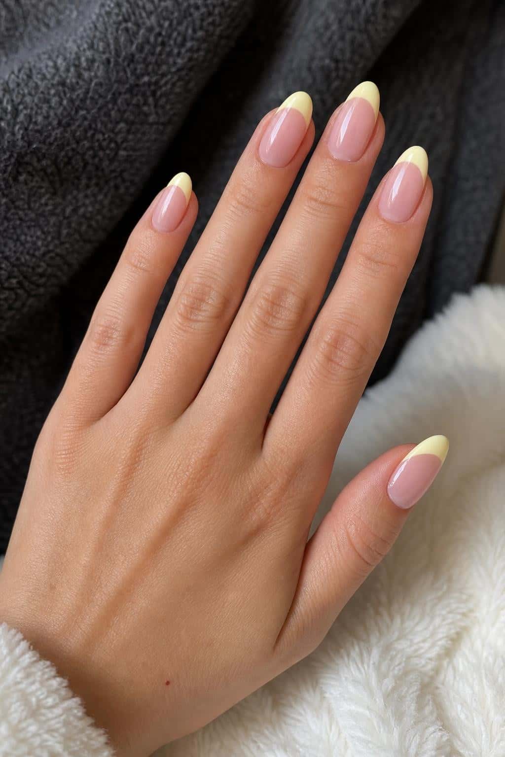 Almond nails with a sheer nude base and pastel yellow French tips in a glossy finish.