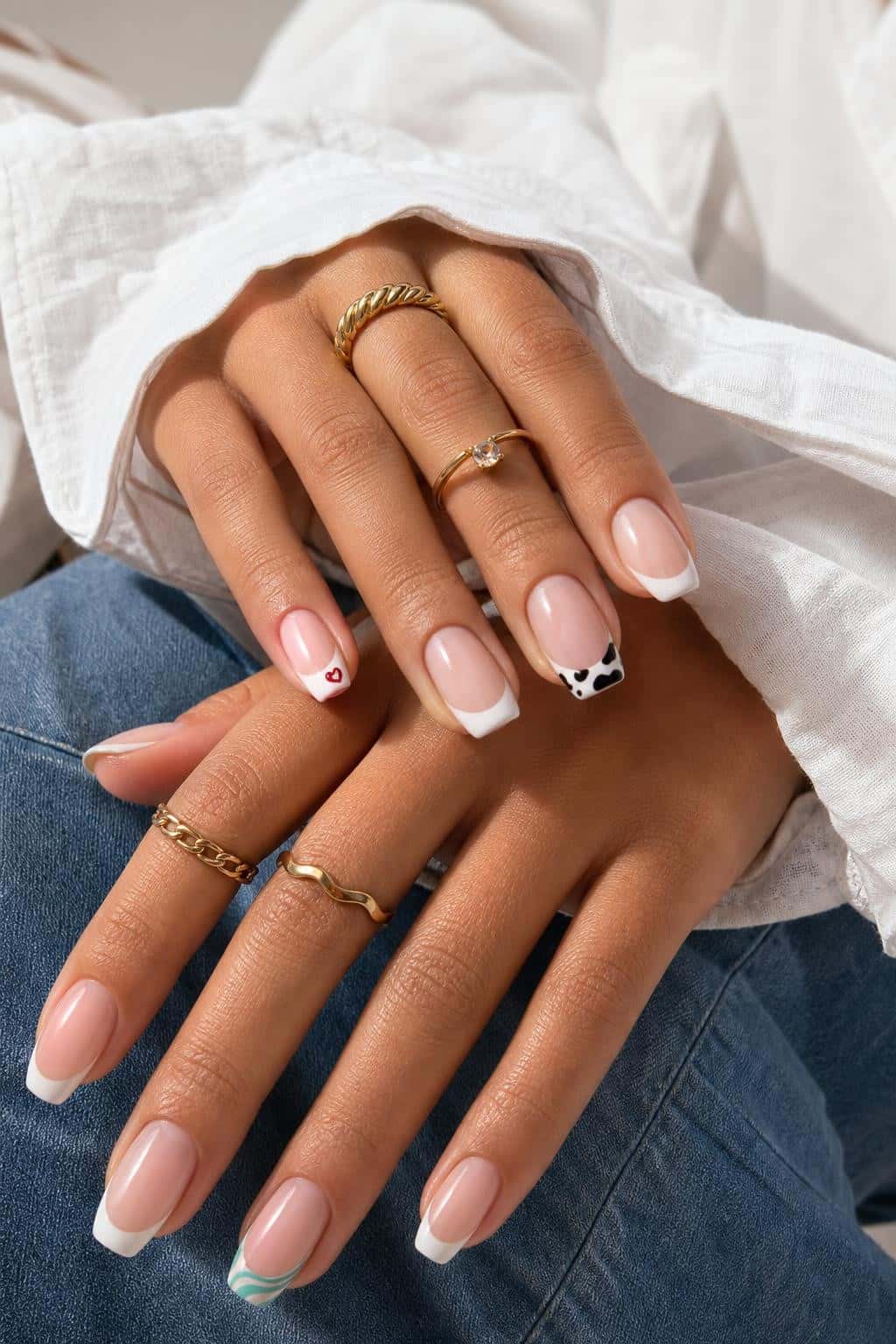 Short squoval nails with classic white French tips, accented with a red heart, cow print, and teal wavy lines.