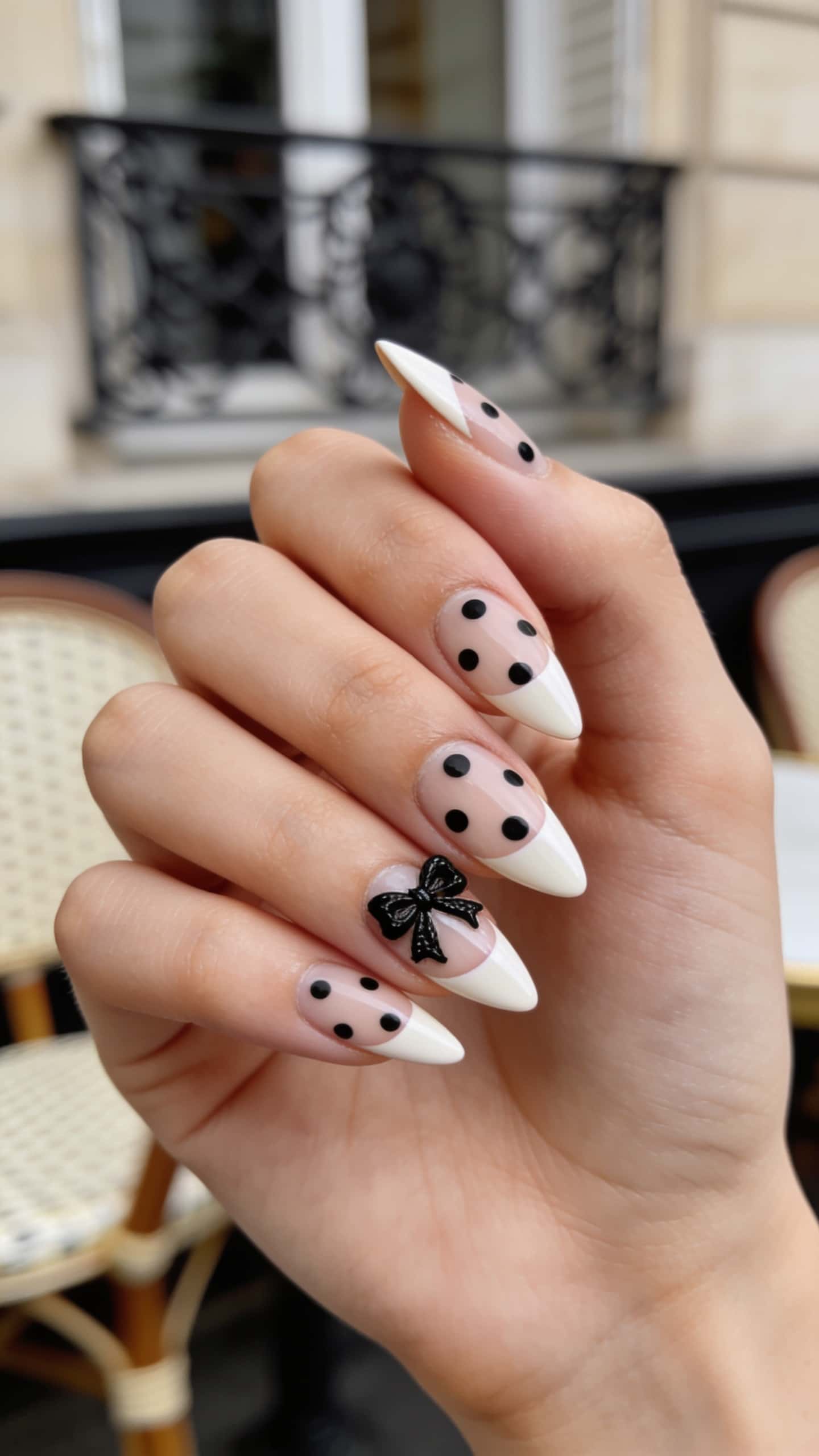 Long stiletto nails with polka dots and 3D bow accents on a nude base and French tip design.