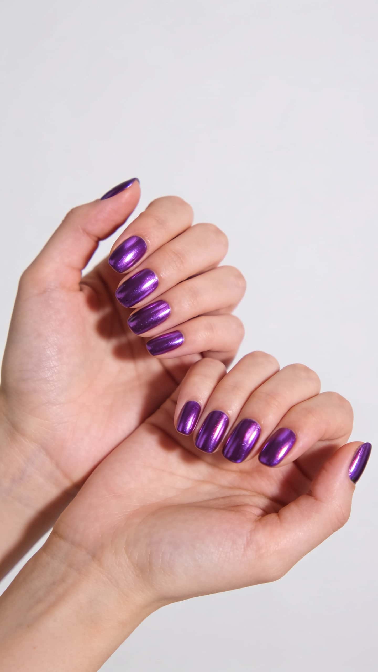 Short oval nails with a vibrant, high-gloss purple chrome finish.