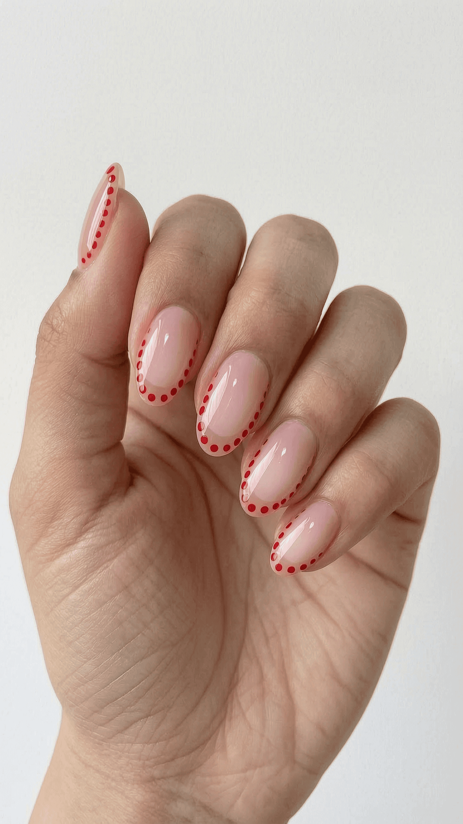 Almond nails with a sheer nude base and a red dot outline design.