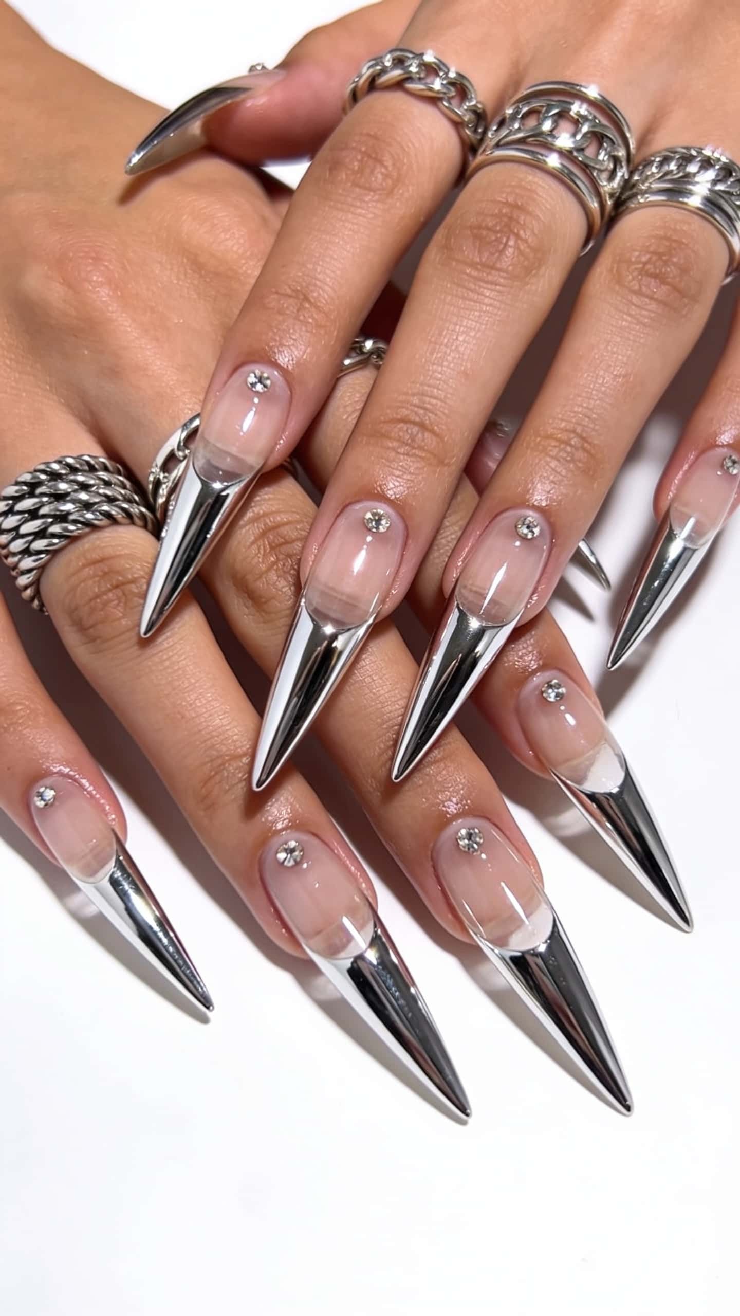 Extra-long stiletto nails with clear bases, sharp silver chrome tips, and a single rhinestone at the cuticle.