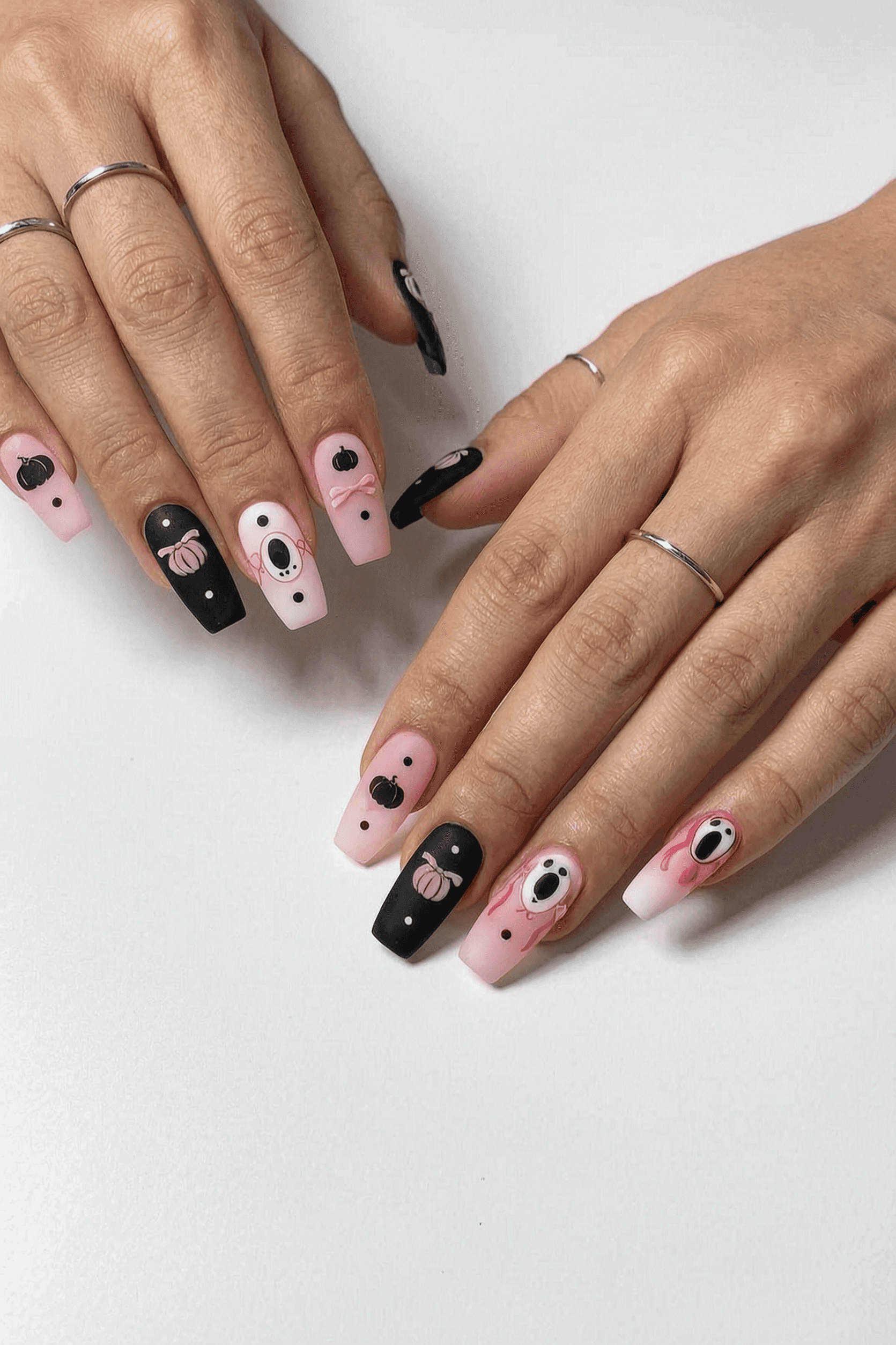 Long coffin nails with a matte finish featuring playful Halloween-themed designs in pink, black, and white.