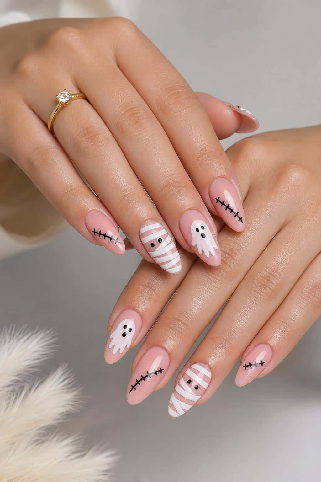 Almond nails with a sheer pink base adorned with playful Halloween ghost, mummy, and stitch nail art.