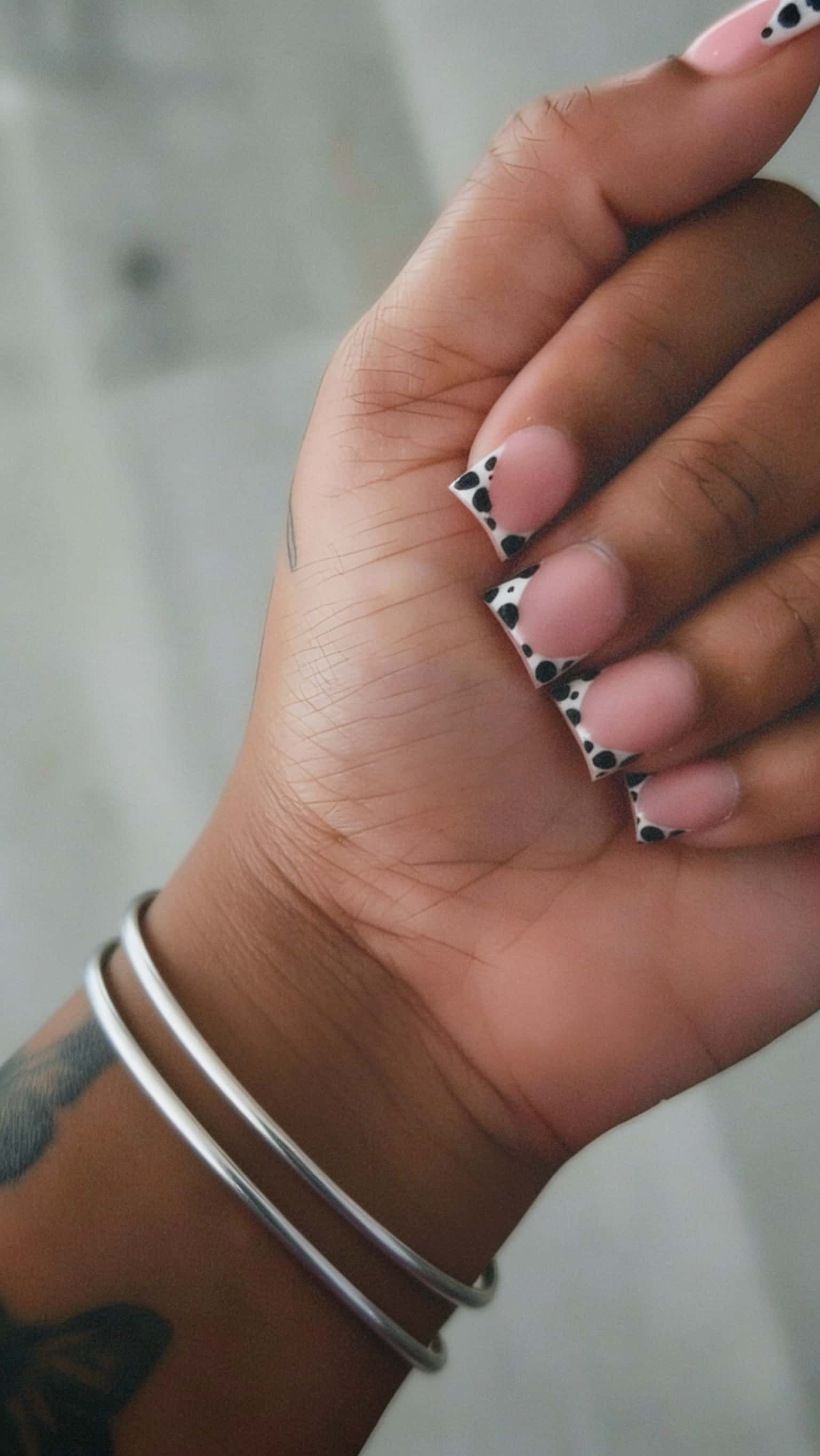 Square nails with a nude base and white French tips featuring black polka dots.