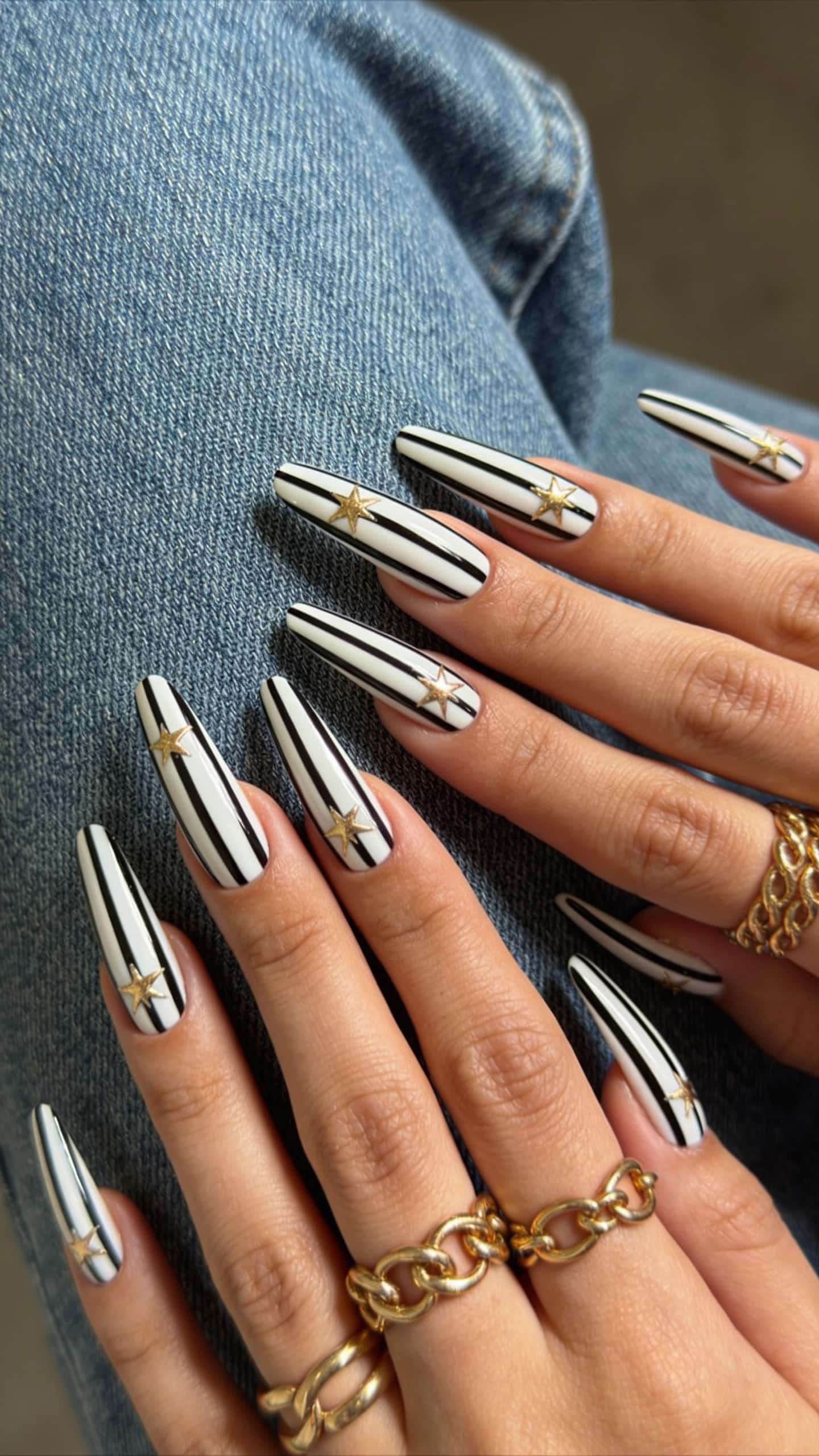 Long stiletto nails with black and white vertical stripes and gold star embellishments.