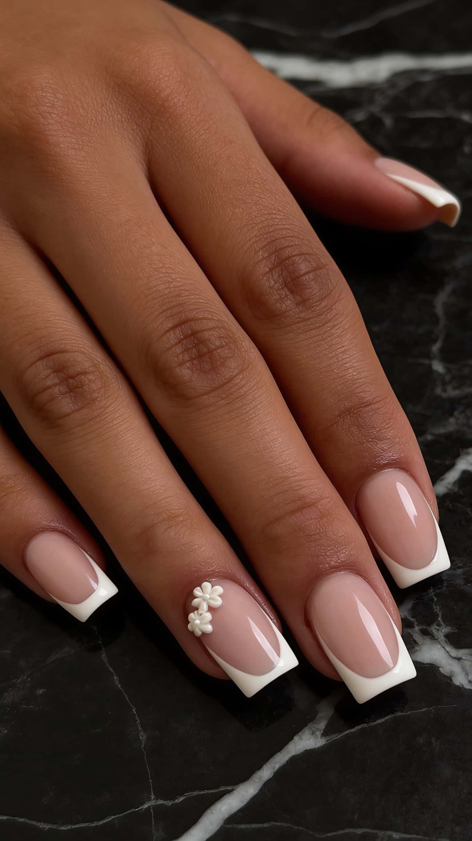 Square nails with a sheer nude base, white French tips, and a delicate 3D white floral accent on the ring finger.