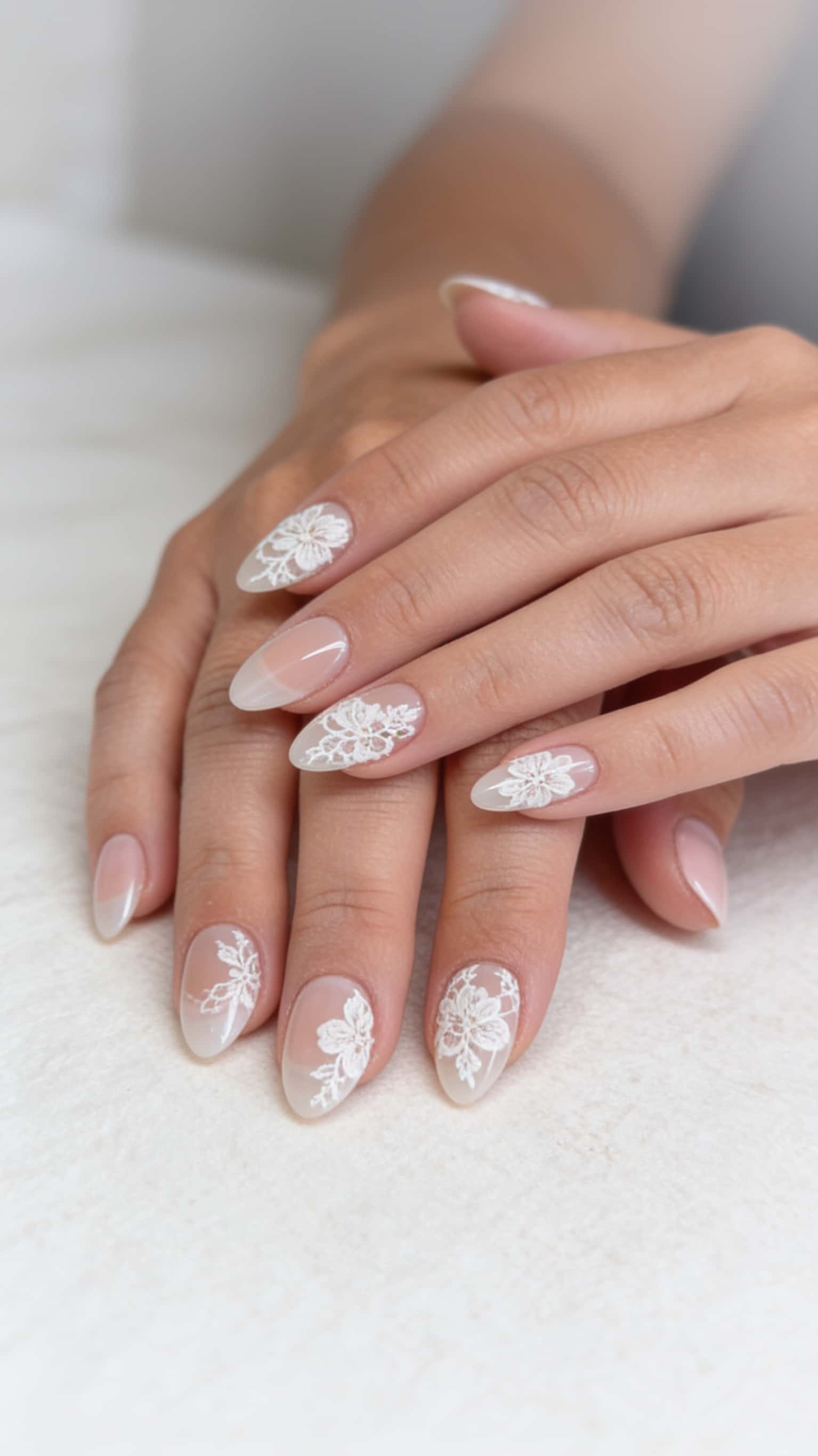 Almond nails with a sheer nude base and delicate white lace floral patterns.