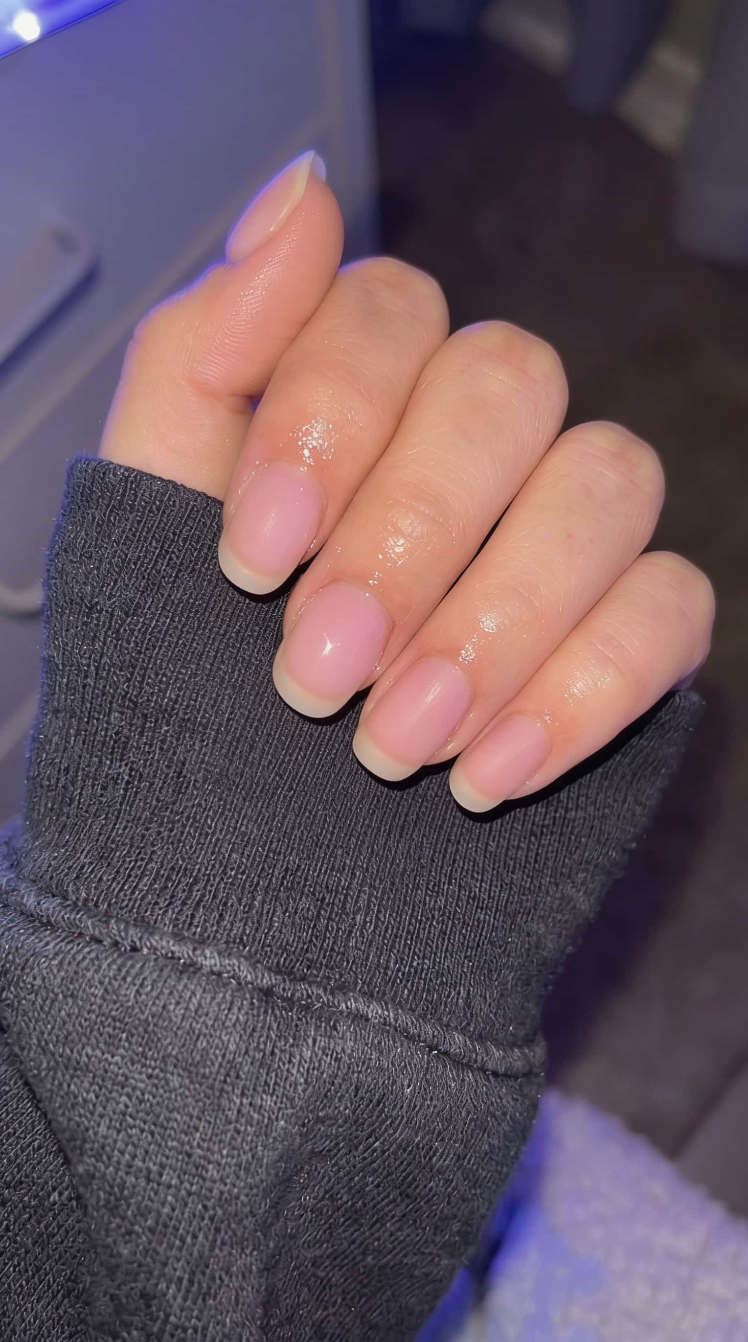 Customer's bare, natural nails before a manicure, posed on a dark sleeve.