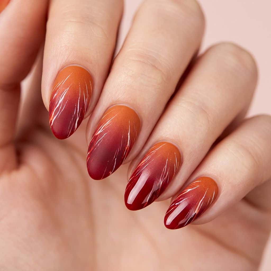 A modern, bold, and radiant nail art design featuring a gradient of burnt orange and deep crimson hues, transitioning from a matte finish at the cuticle to a.
