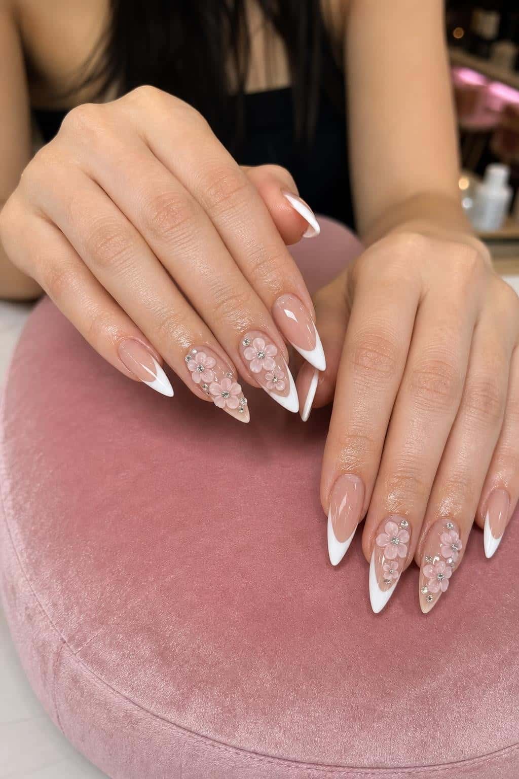 Long stiletto nails with nude and white French tips, accented with 3D pink flowers and rhinestones.