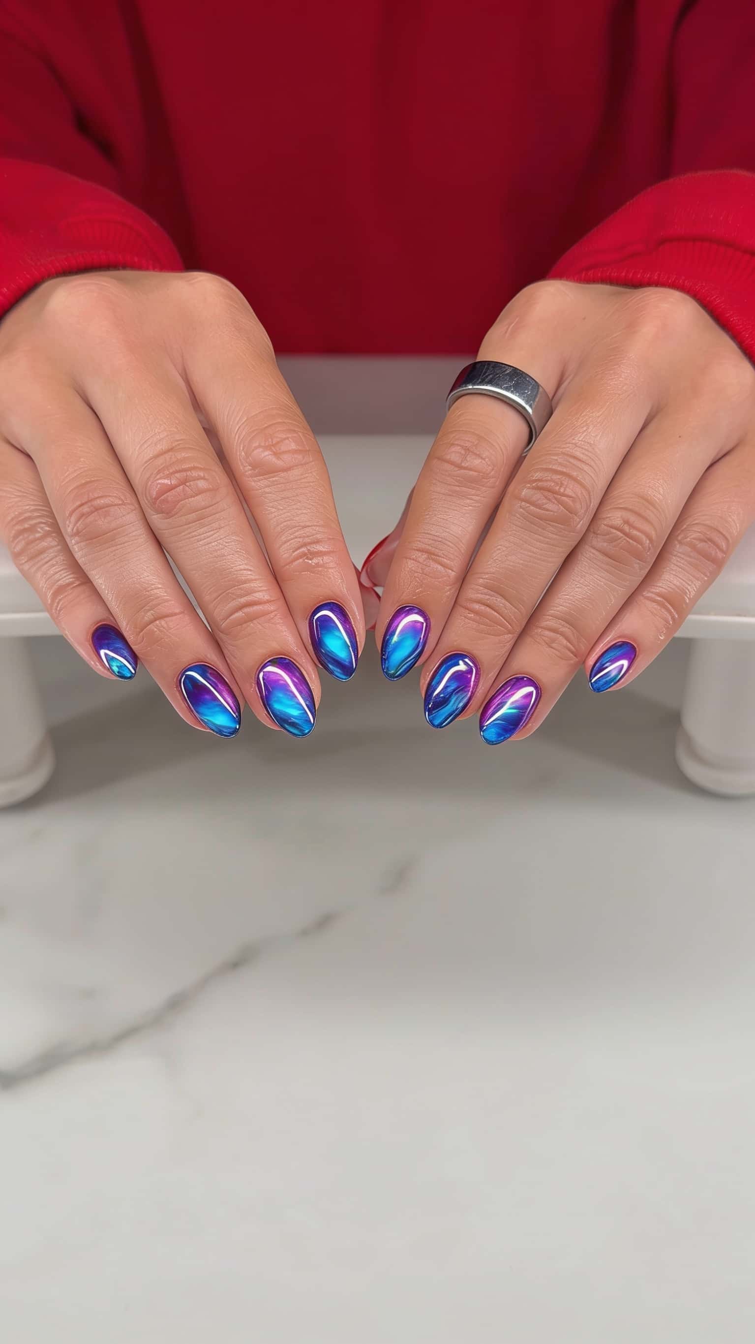 Short oval nails with a high-gloss, swirling iridescent aurora effect in blues, purples, and magentas.