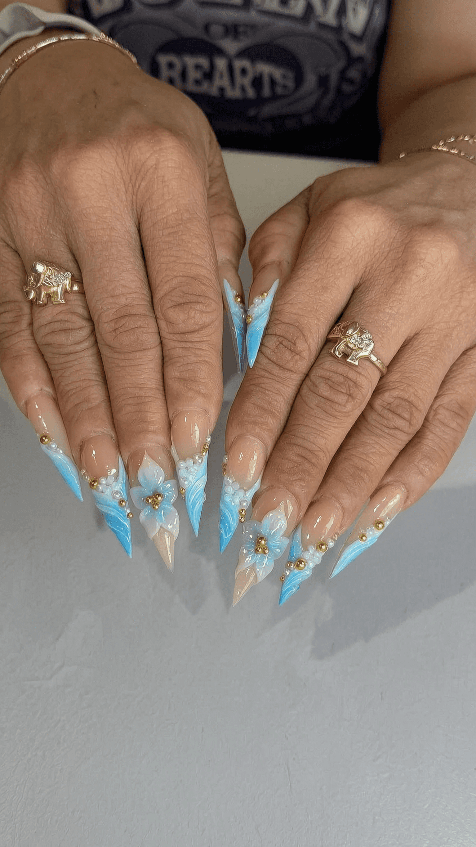 Long blue ombre stiletto nails with 3D floral accents and gold beads.