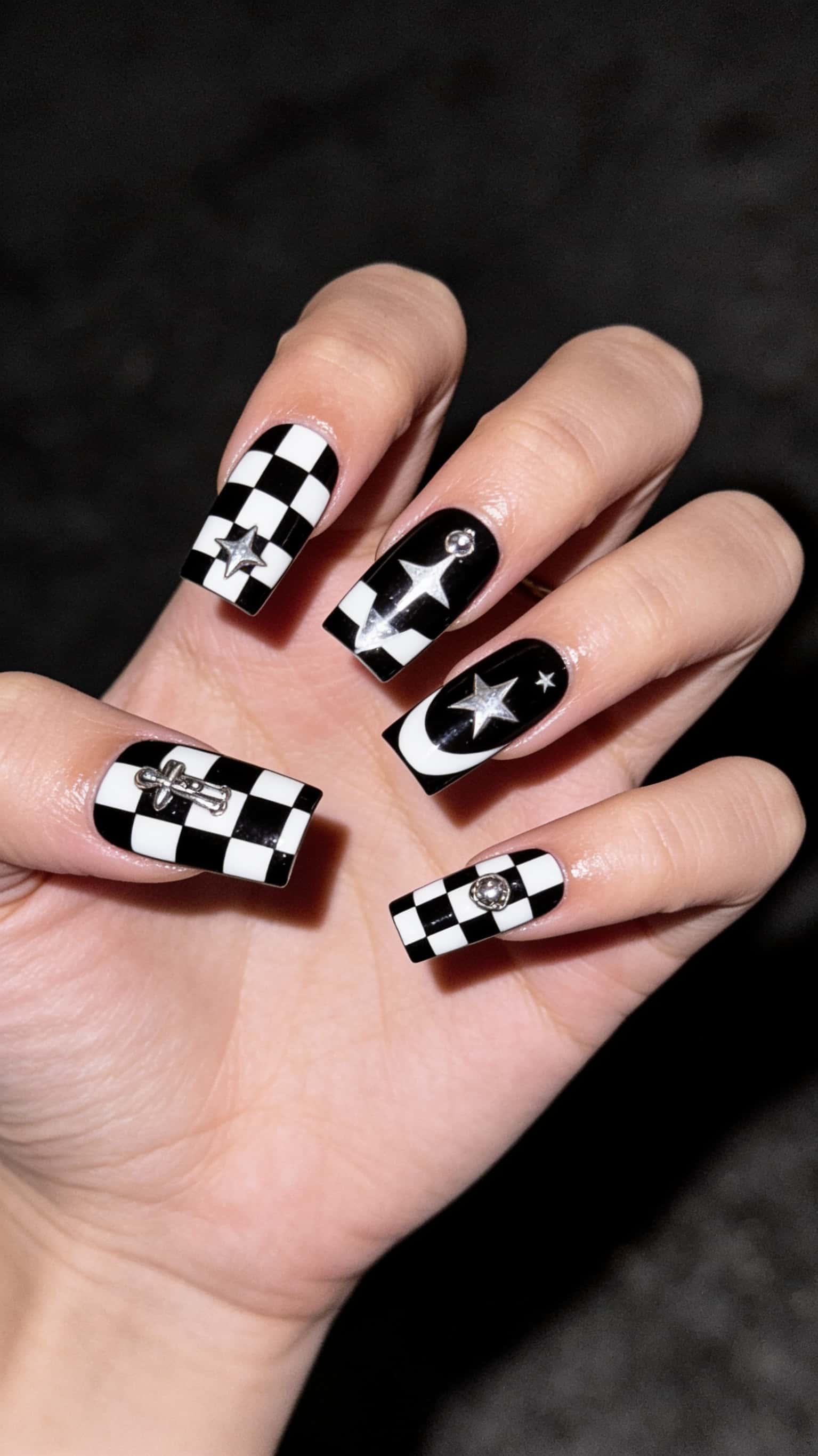 Long square nails with black and white checkerboard and celestial patterns, adorned with silver 3D charms and rhinestones.