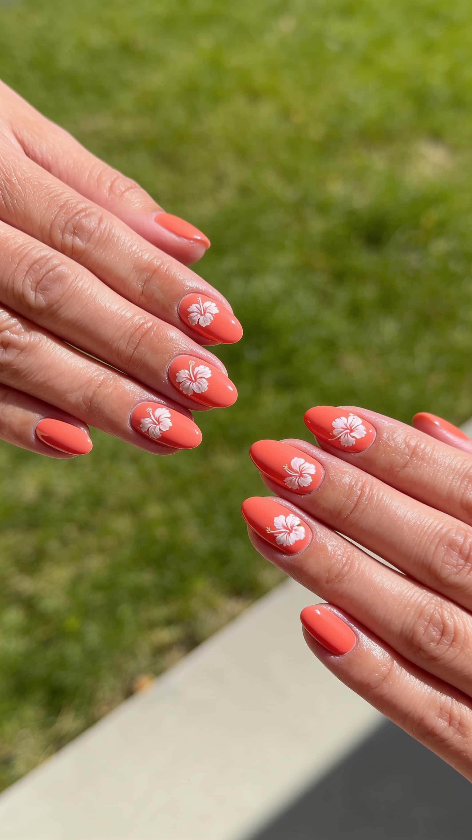 Oval coral nails adorned with white hibiscus flower designs and a glossy finish.