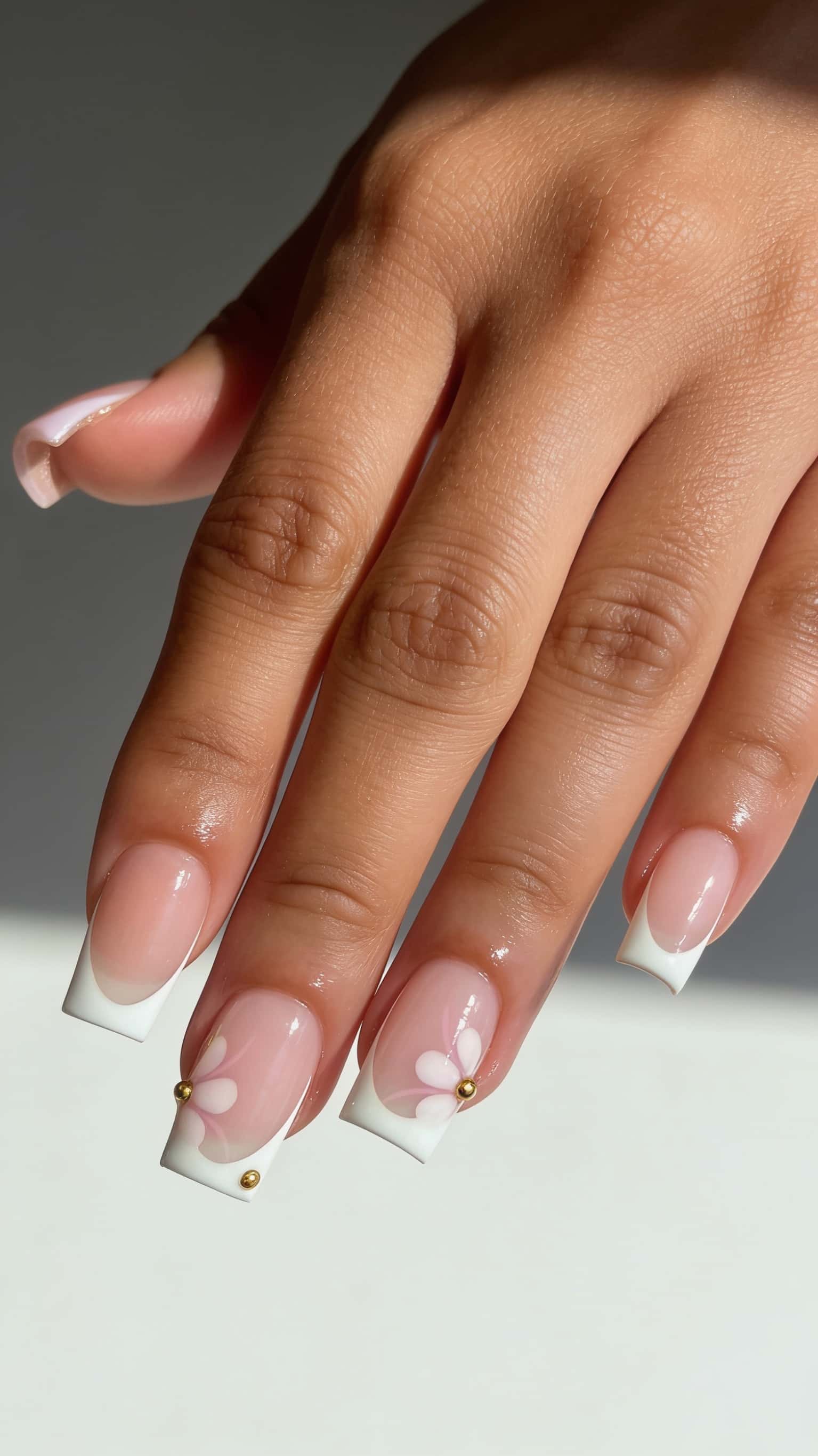 Medium square nails with nude base, white French tips, and white floral designs with gold studs on accent nails.