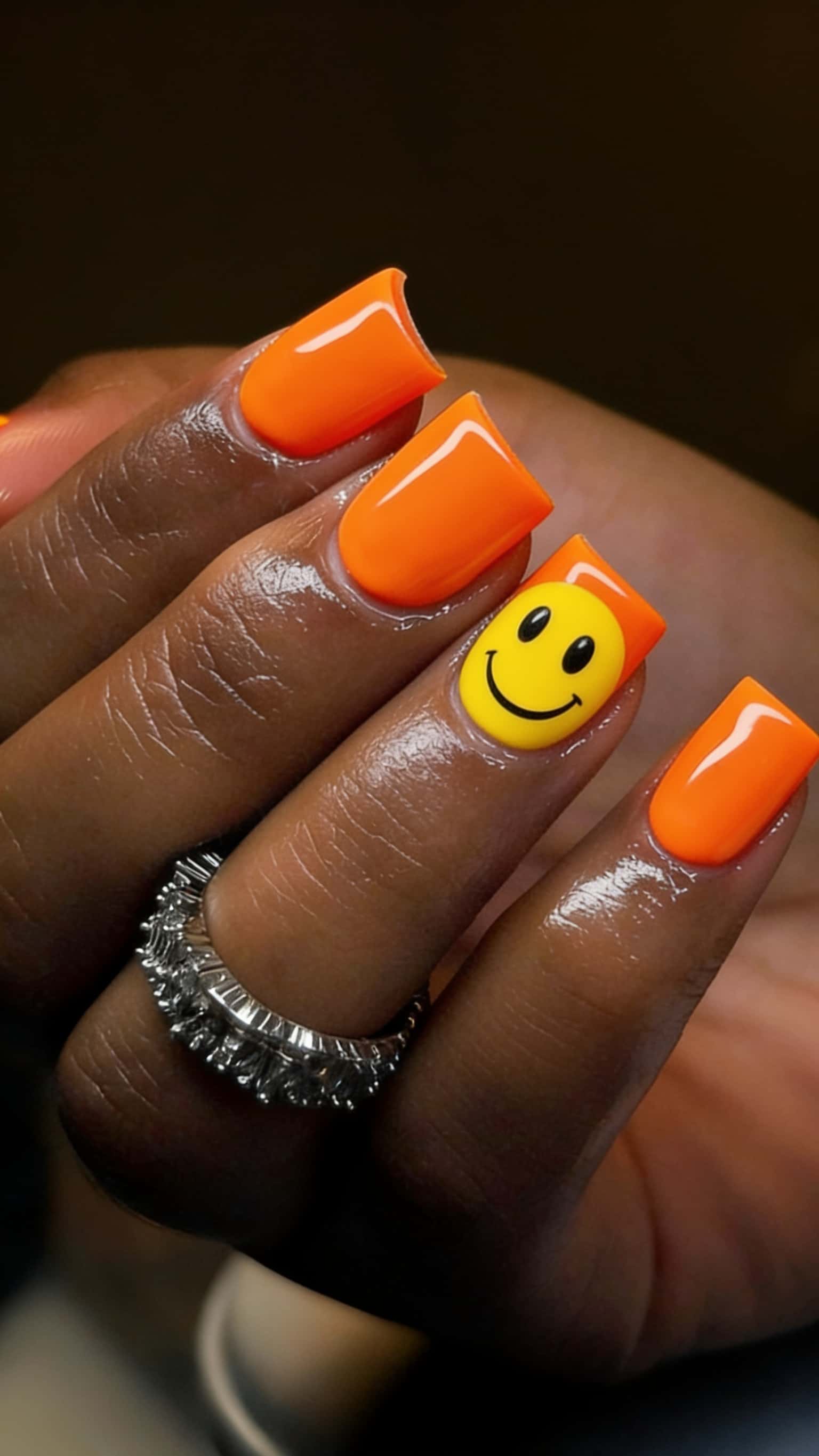 Short square nails with a neon orange glossy finish, featuring a 3D yellow smiley face on the ring finger.