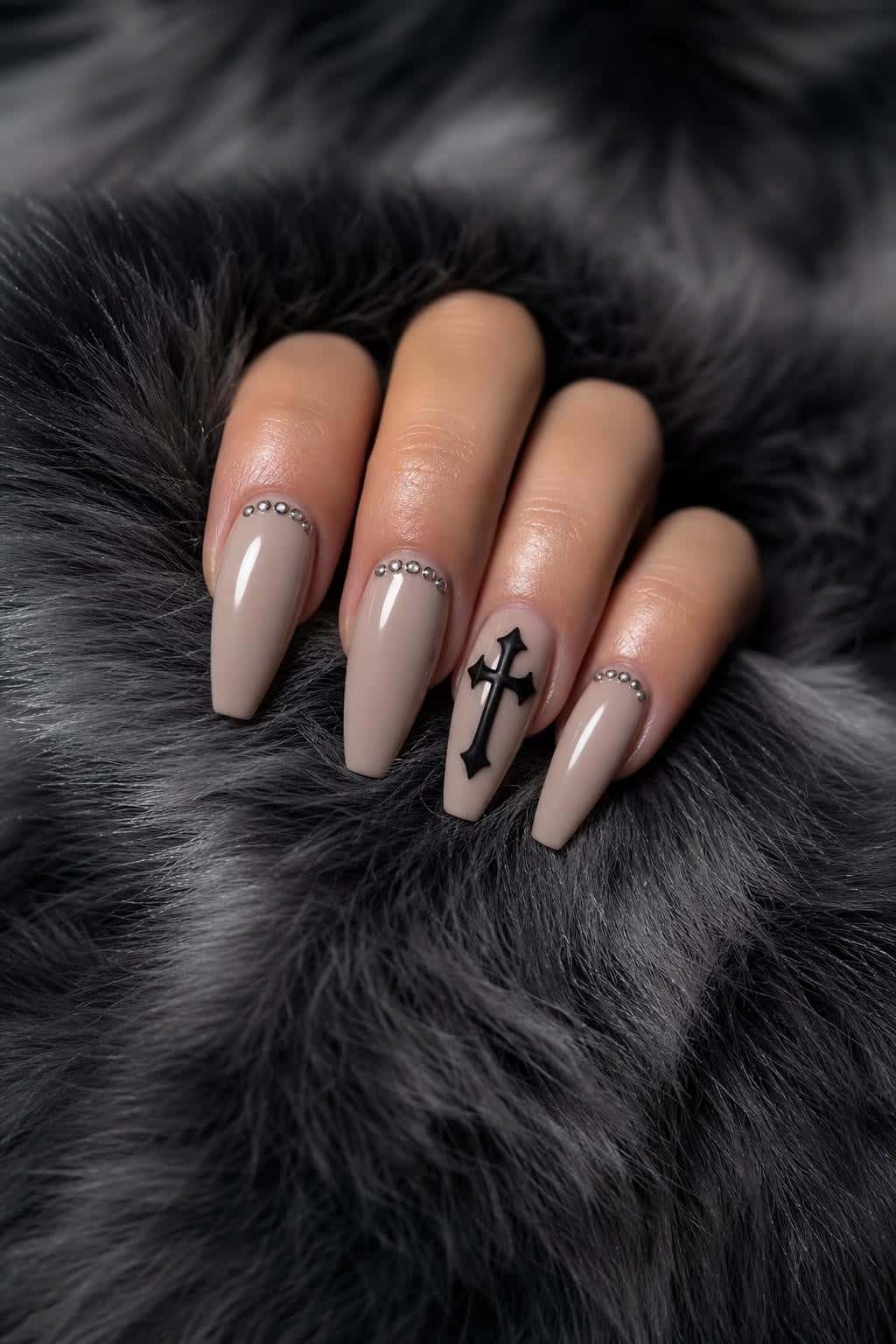Long coffin nails with nude base, 3D black cross, and rhinestones.