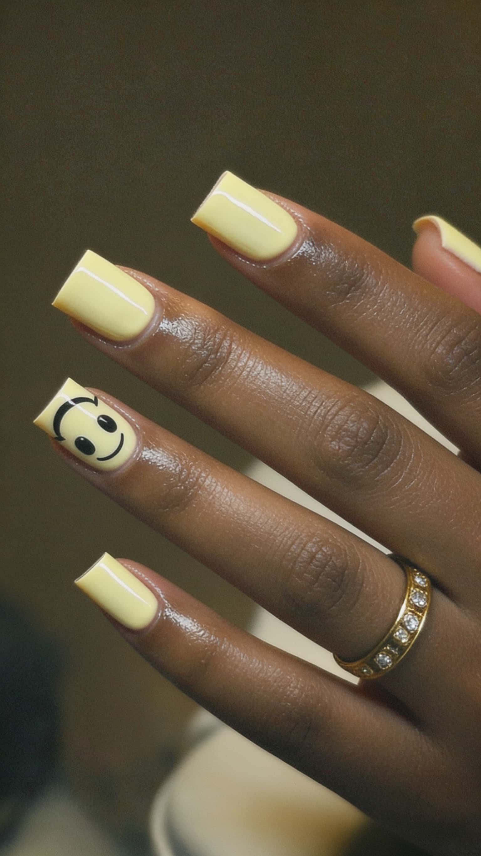 Glossy pastel yellow square nails with a black smiley face accent on one finger.