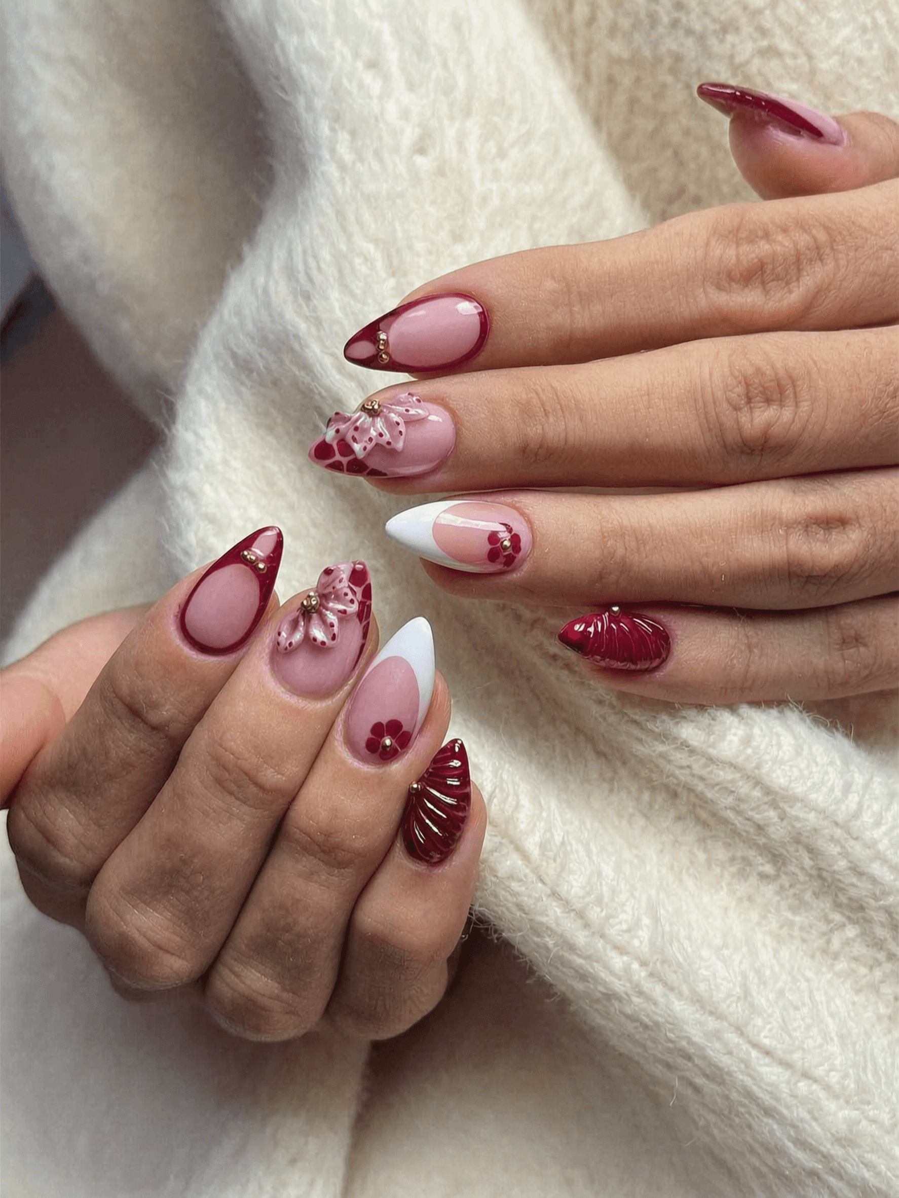 Long red stiletto nails with gold accents and glossy finish, featuring 3D floral design.