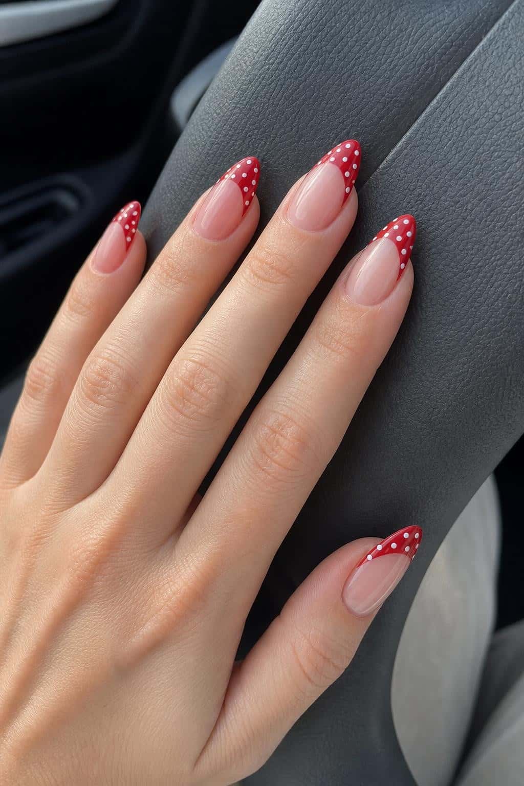 Almond nails with a nude base and red French tips featuring white polka dots.