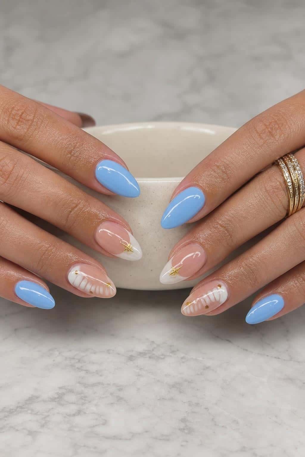 Almond nails with a playful mix of solid sky blue, nude and white V-French tips, and gold star and dot accents.