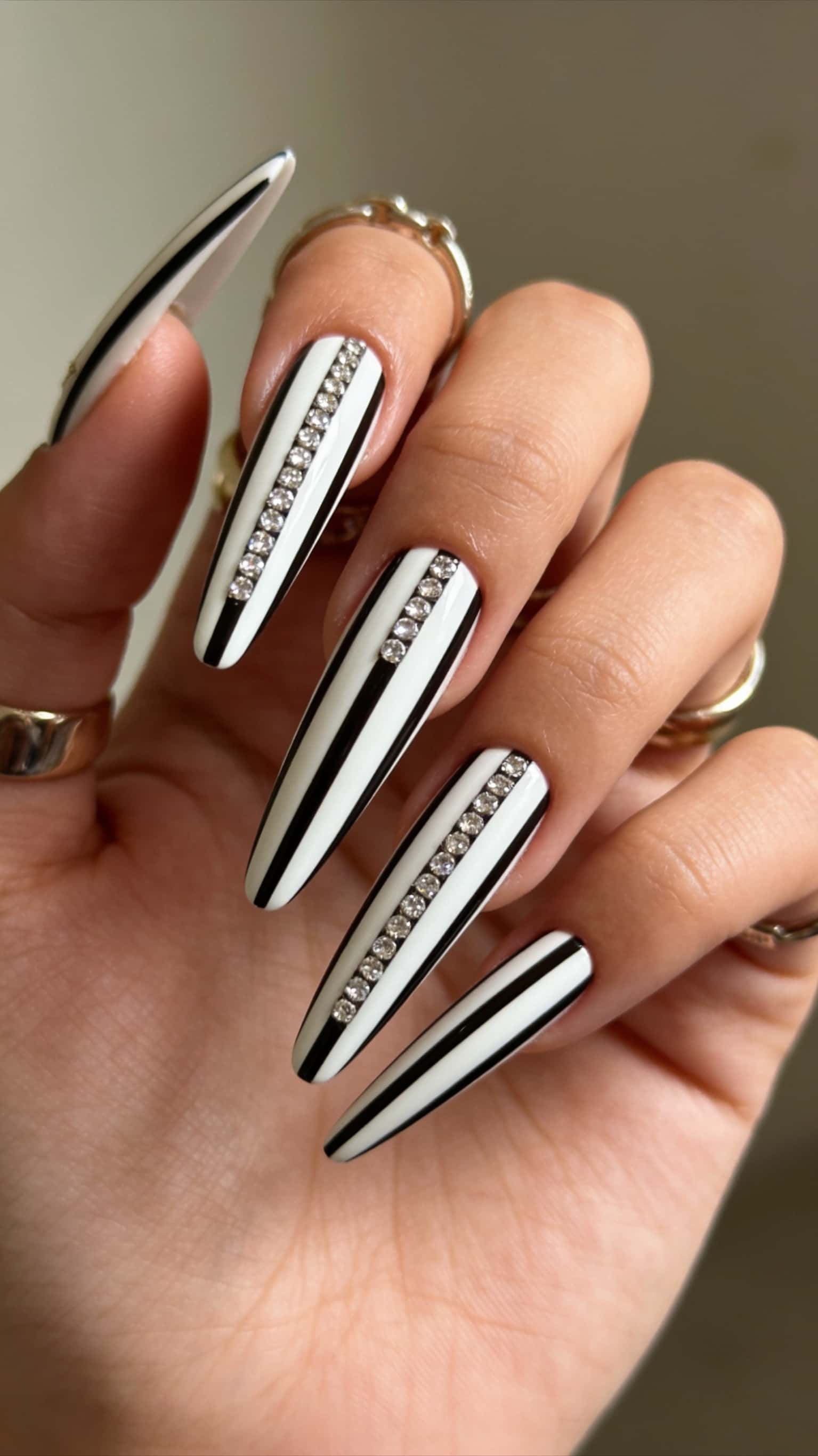 Long coffin nails with black and white vertical stripes and a central line of clear rhinestones.