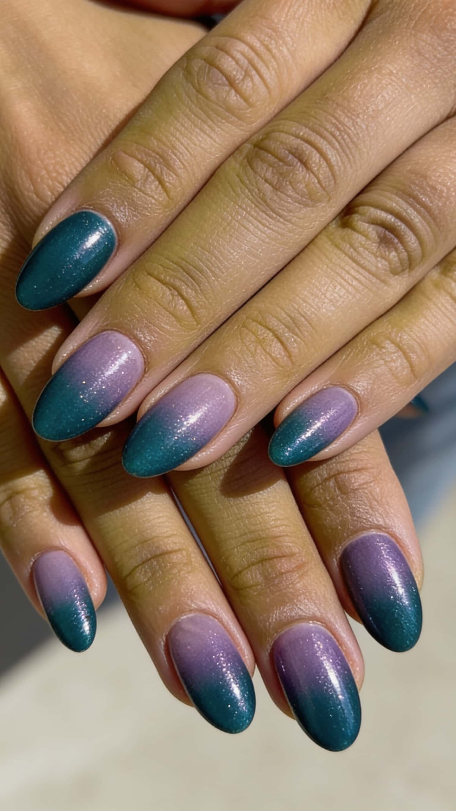 Oval nails with a glitter ombre fading from dark teal to lavender.