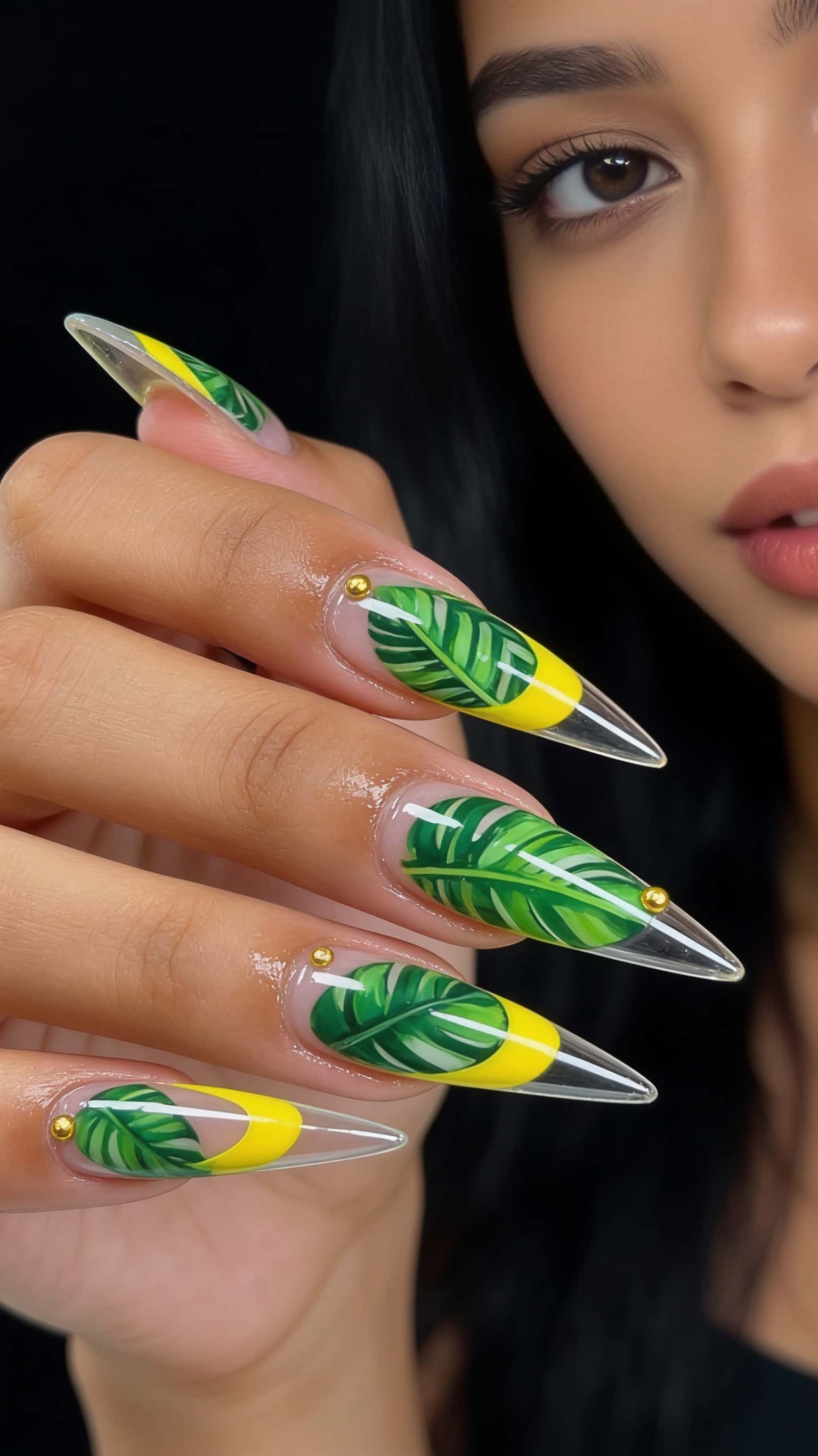 Long stiletto nails with tropical leaves design, yellow accent, and gold studs.
