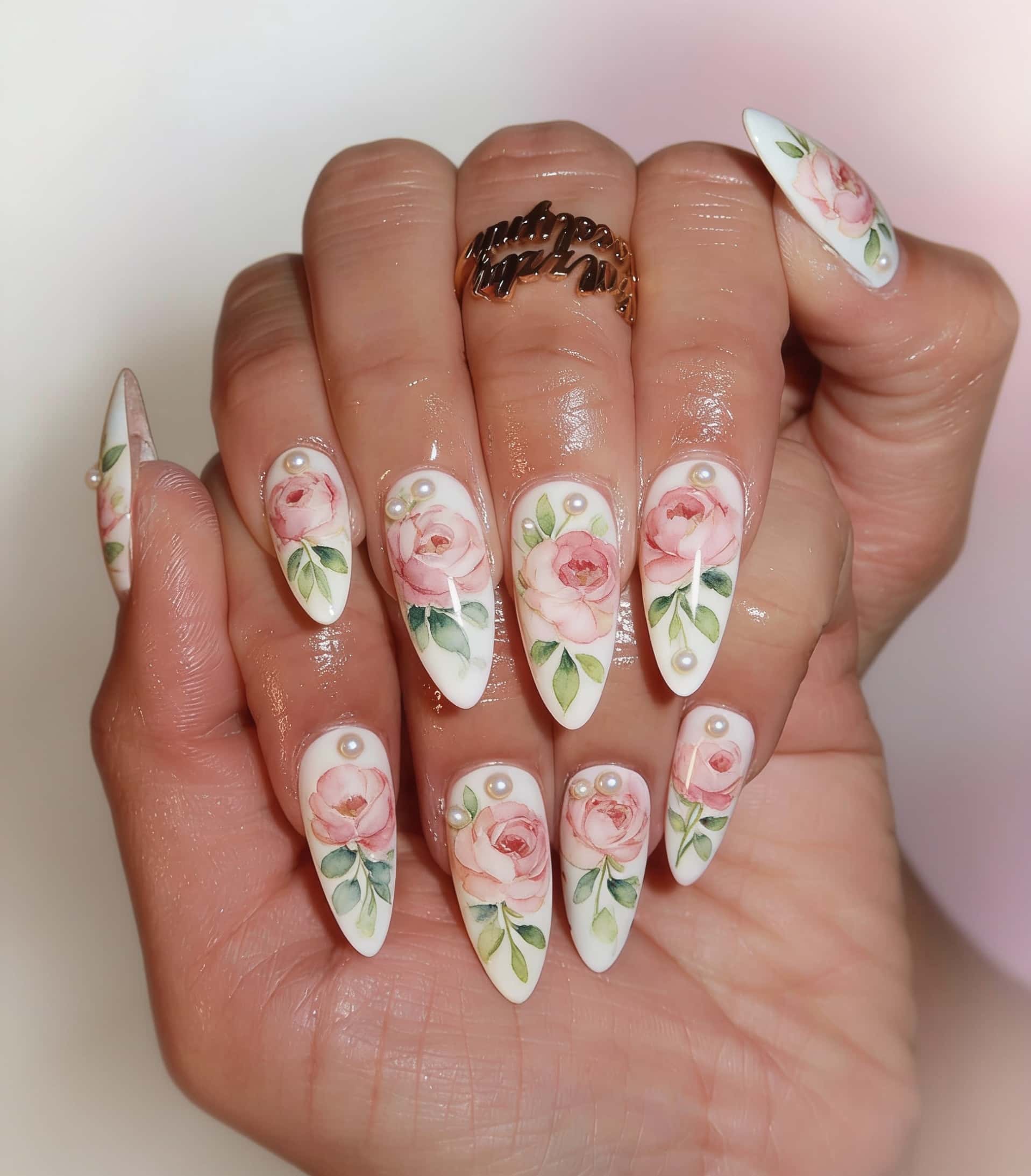 Long stiletto nails with watercolor pink roses and green leaves on a white base, accented with small pearls.